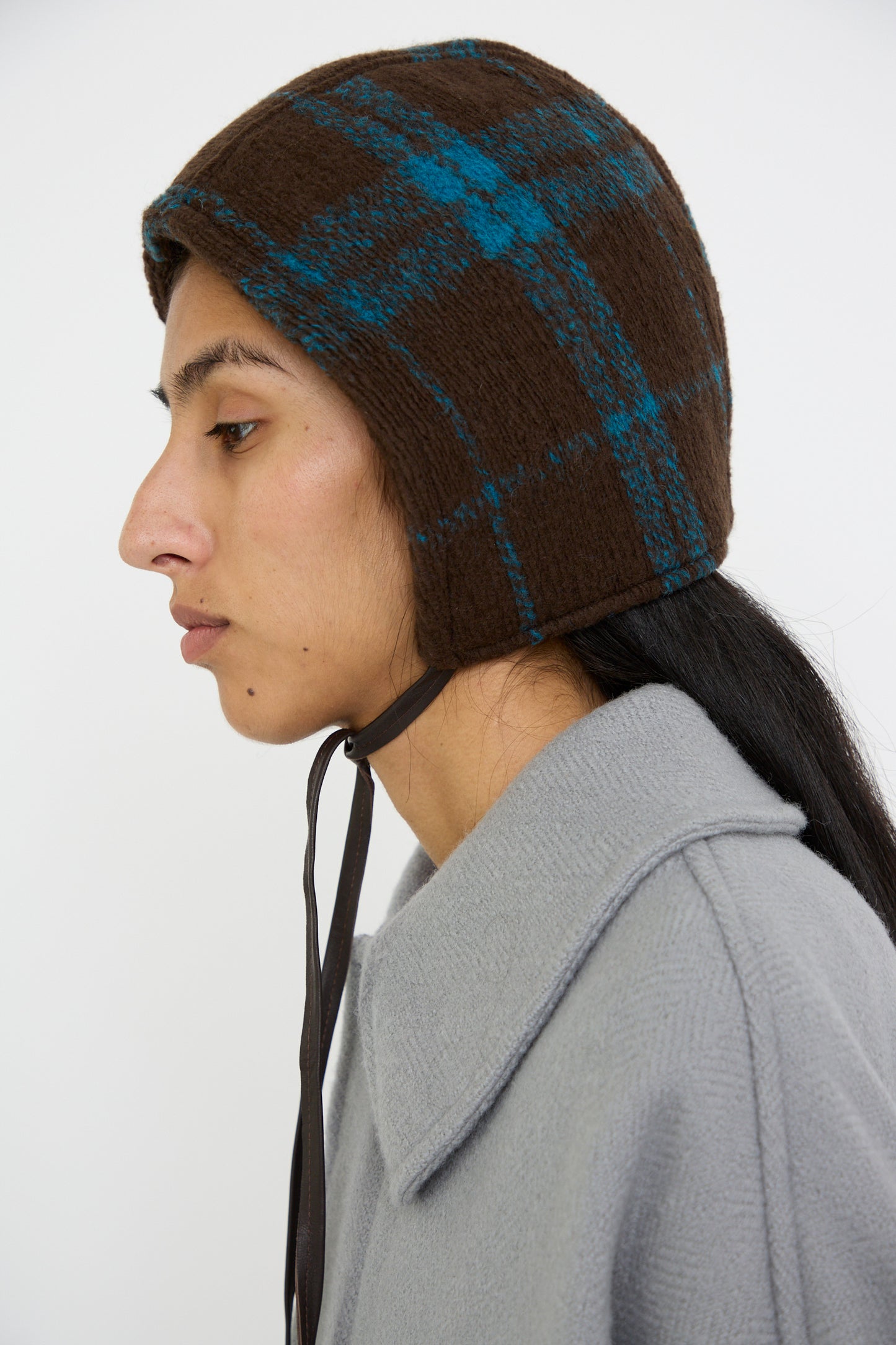 A person in profile wears a gray coat wears the Clyde Volo Hat in Brown Electric Plaid with chin straps, looking to the left.