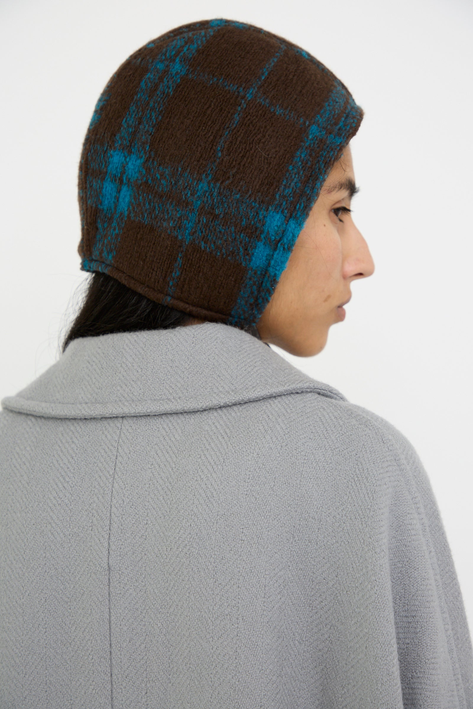 A person wearing a Volo Hat in Brown Electric Plaid by Clyde and a light gray coat is seen from the back.