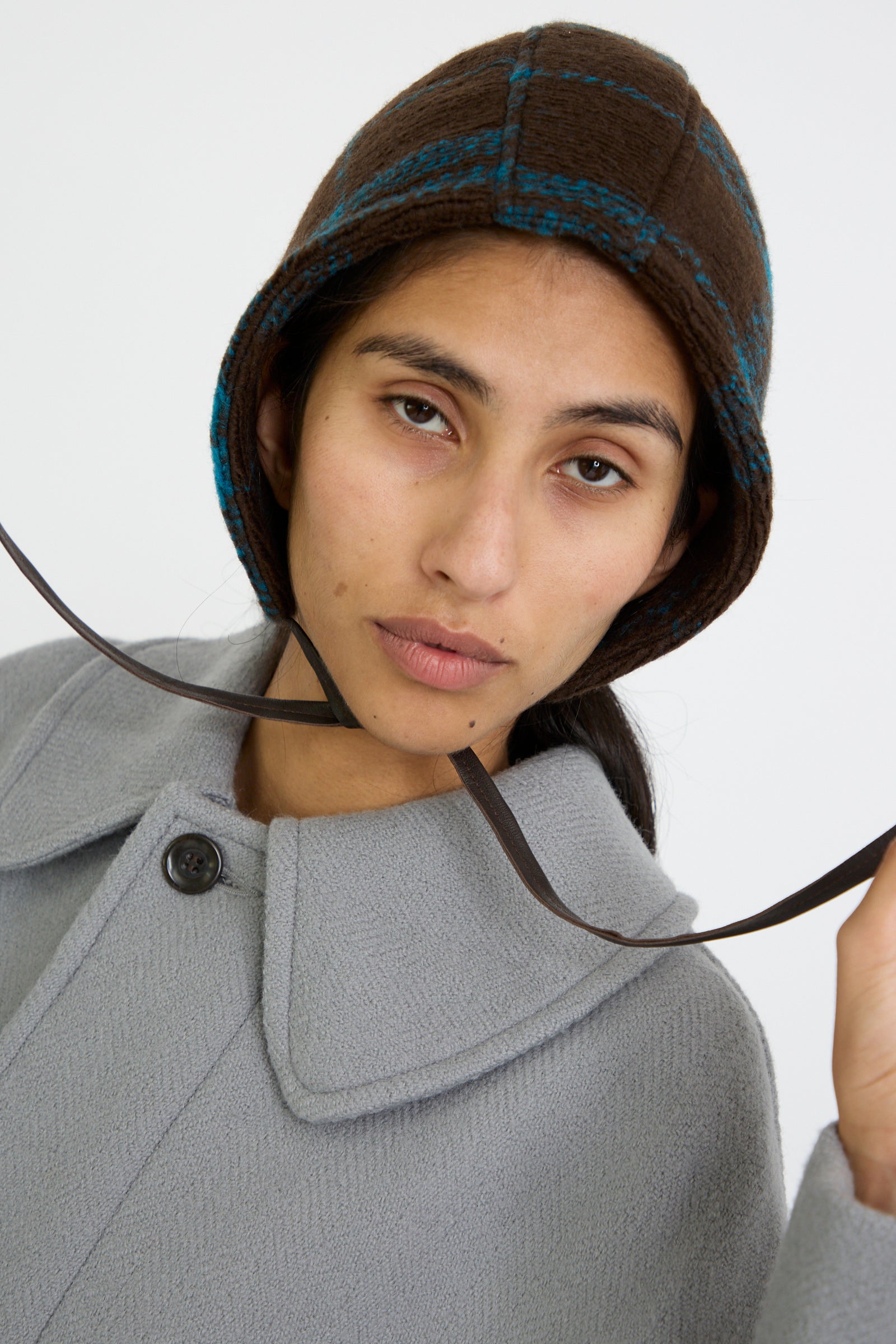 A person looks forward, wearing a gray coat and the Clyde Volo Hat in Brown Electric Plaid,  against a plain white background.