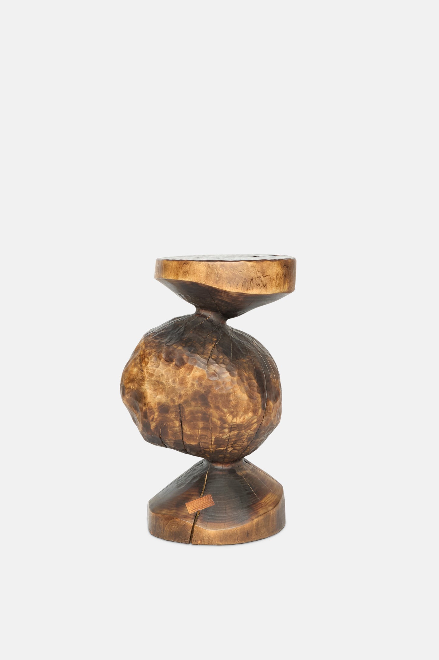 The Bon Bon Side Table by Cody Brgant is a hand-carved wooden stool inspired by Japanese pagodas, featuring a round, uneven center and natural cracks, shown against a plain white background.