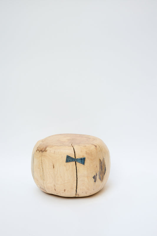 The Fort Greene Maple Pouf, crafted from a natural maple tree, showcases a blue butterfly joint repair on its crack. Handmade in Brooklyn by Cody Brgant, it stands elegantly against a plain white background.