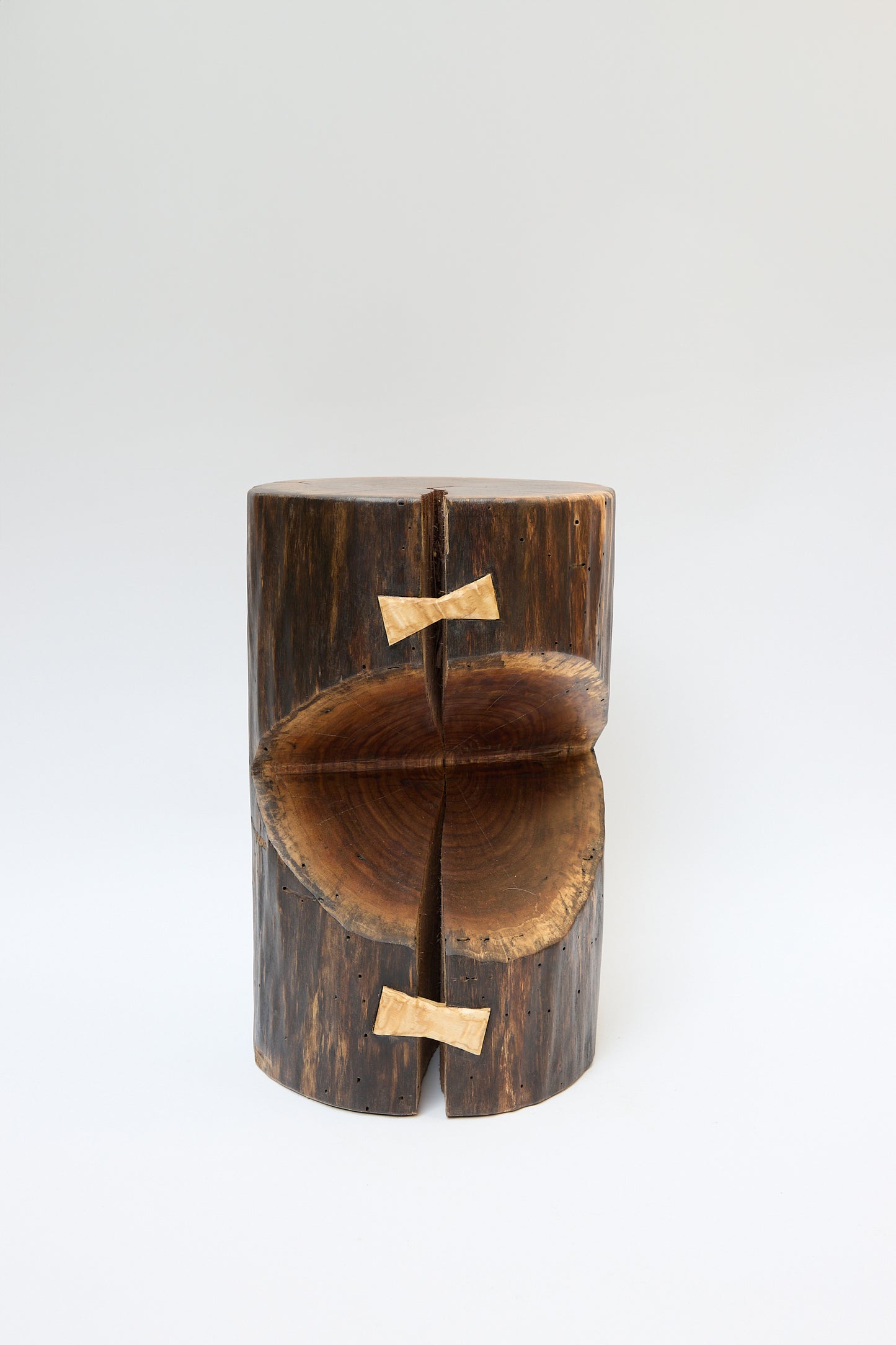 A wooden log stool, crafted from a walnut tree and split in half, is held together with two wooden W-shaped joints on a plain white background. This Kingston Walnut VI Side Table by Cody Brgant exemplifies the artistry of Brooklyn furniture design.