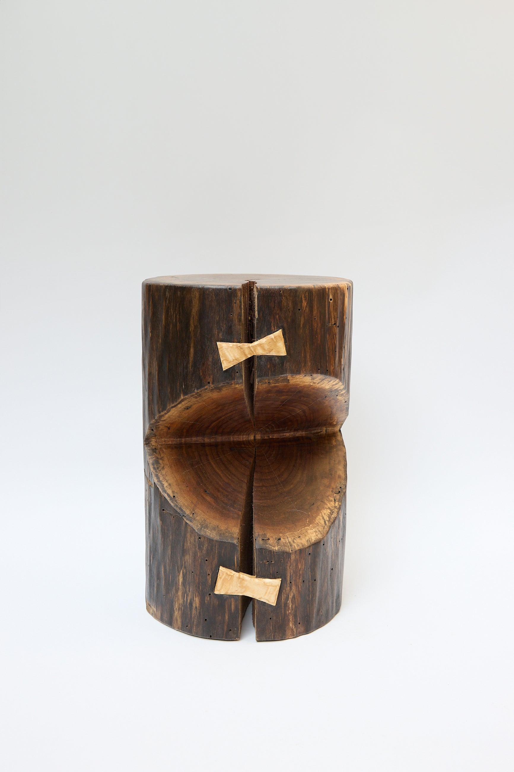 A wooden log stool, crafted from a walnut tree and split in half, is held together with two wooden W-shaped joints on a plain white background. This Kingston Walnut VI Side Table by Cody Brgant exemplifies the artistry of Brooklyn furniture design.