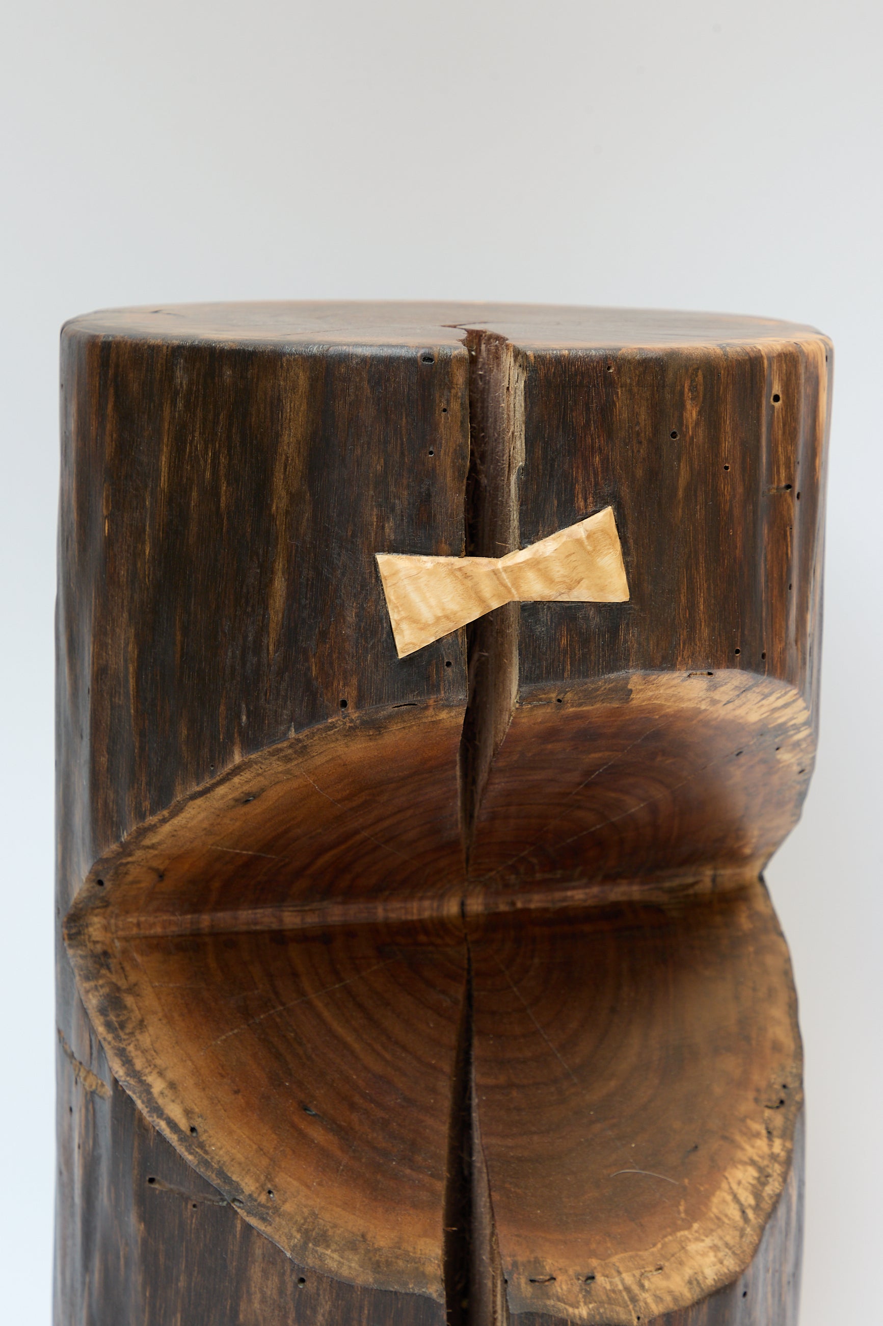 A close-up of a wooden log from a walnut tree with a visible crack, repaired with a light-colored bowtie-shaped inlay. This Cody Brgant Kingston Walnut VI Side Table showcases natural grain patterns, set against a plain background, embodying the artistry of a handmade side table.