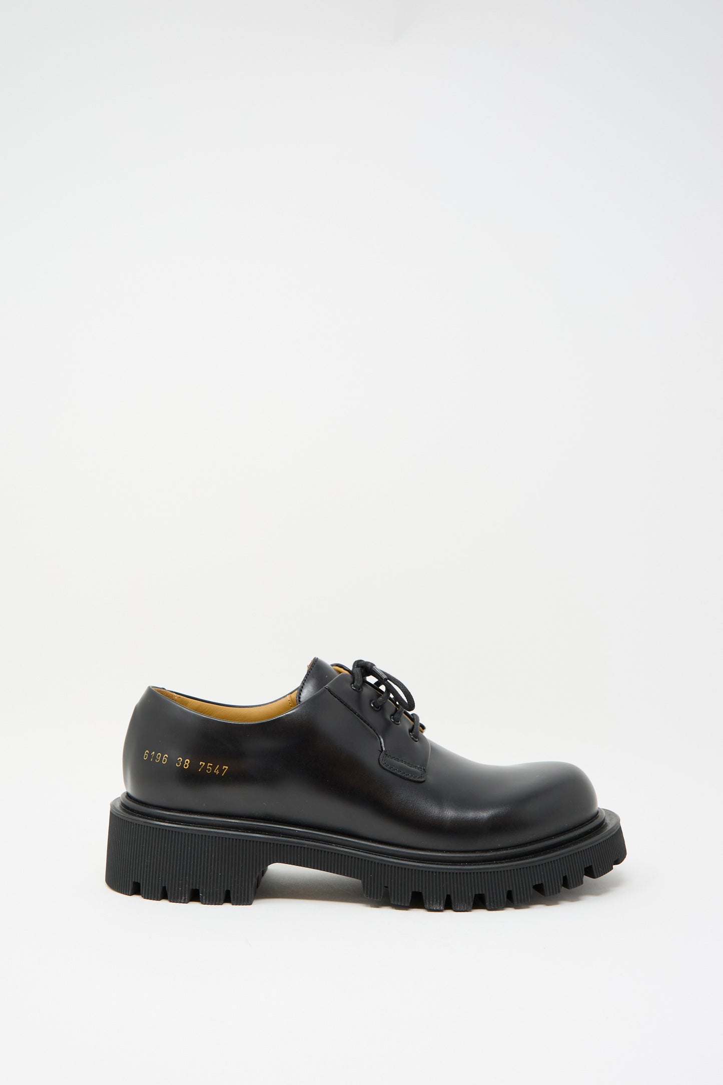 The Chunky Derby 6196 in Black by Common Projects is a chunky leather shoe featuring a rubber lug sole, lace-up design, and side numbers.