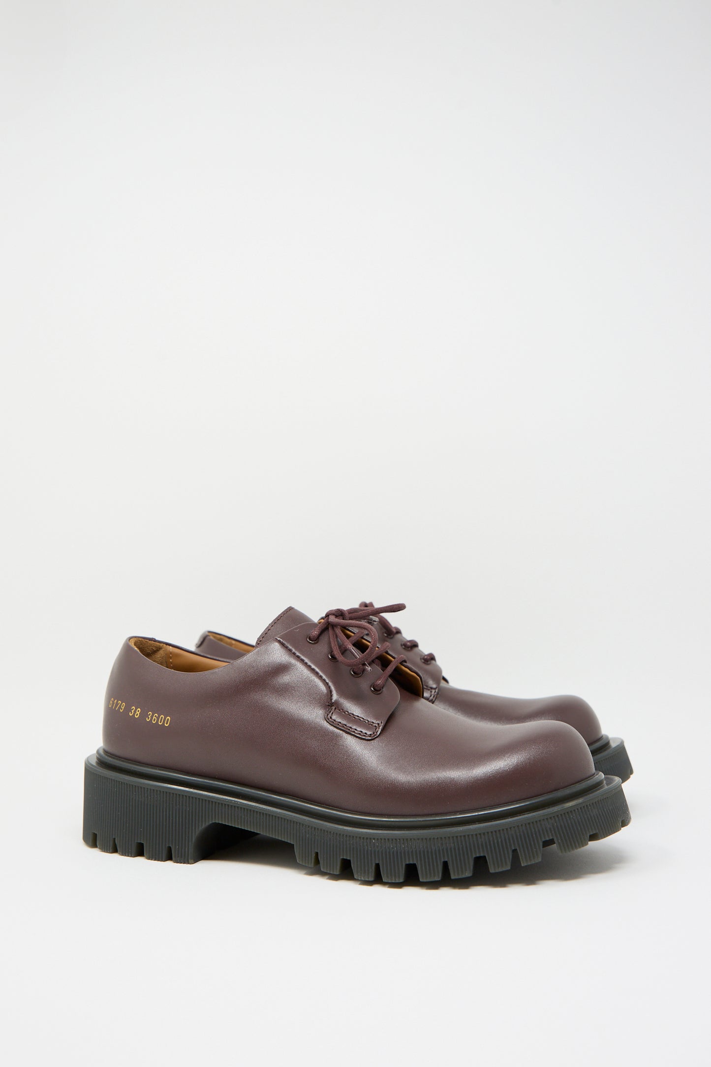 The Common Projects Chunky Derby Article 6179 in Burgundy with Gum is a pair of Italian-made leather shoes featuring thick black rubber soles and distinctive gold numbering on the side.