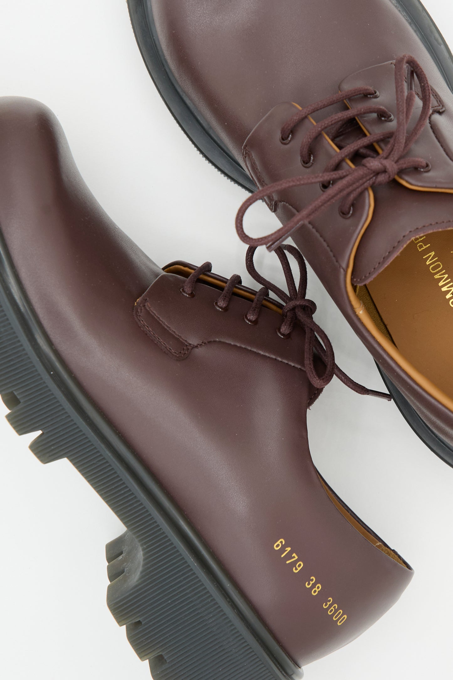 A pair of Chunky Derby shoes in burgundy leather with gum soles from Common Projects. The numbers "6179 38 3600" are printed in gold on the side of one shoe. Made in Italy, these shoes combine style and elegance seamlessly.