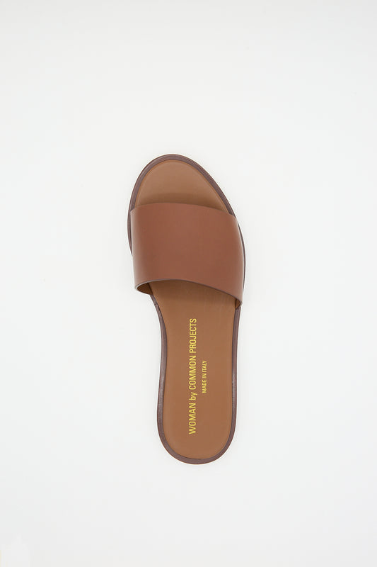 A luxury Common Projects Leather Slide 6155 Sandal in Brown displayed against a white background.