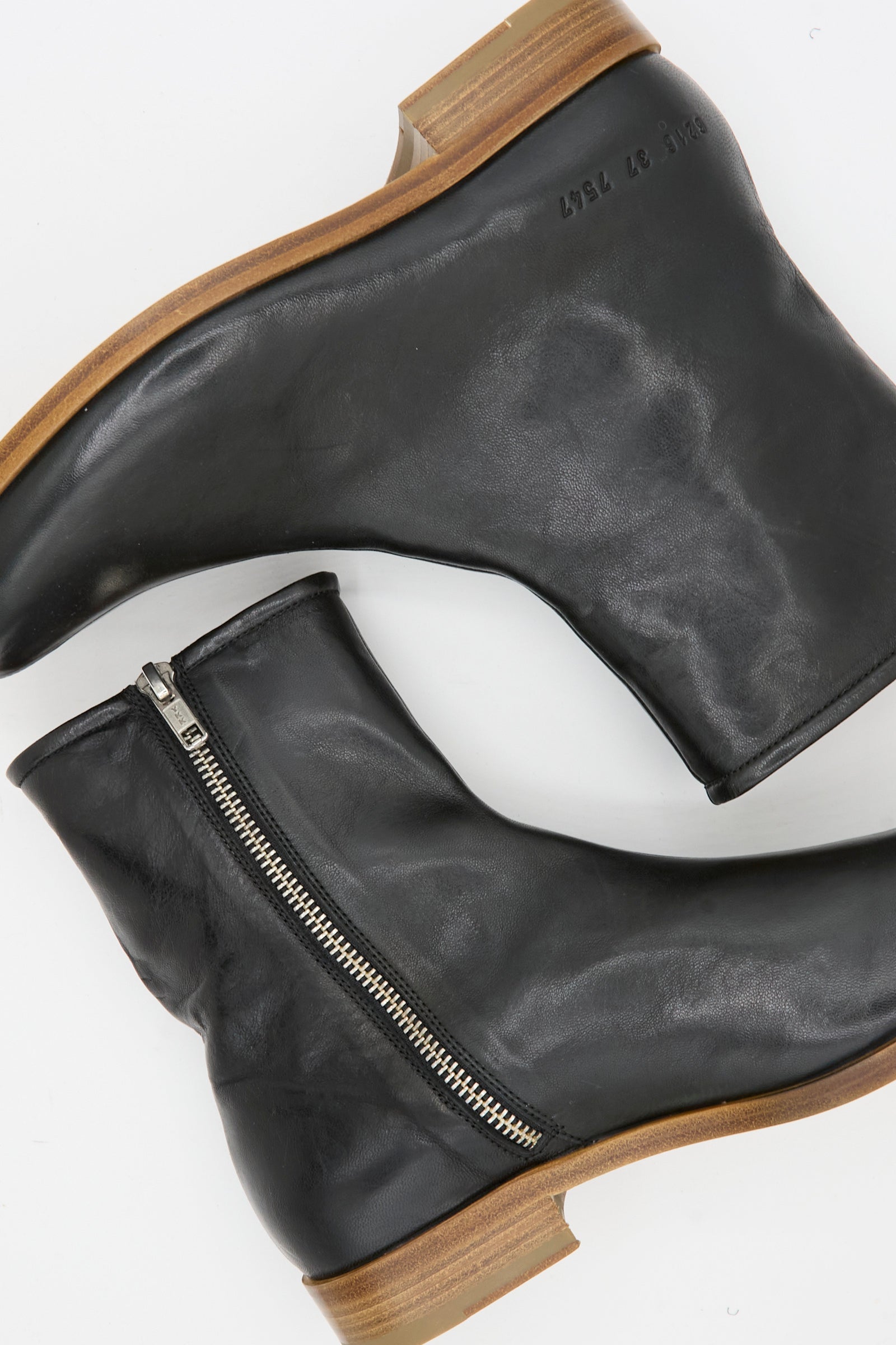 The Common Projects Zipper Boot Article 6216 in Black, made in Italy, features black leather, side zippers, and light brown wooden soles. Shown laid on a white background.