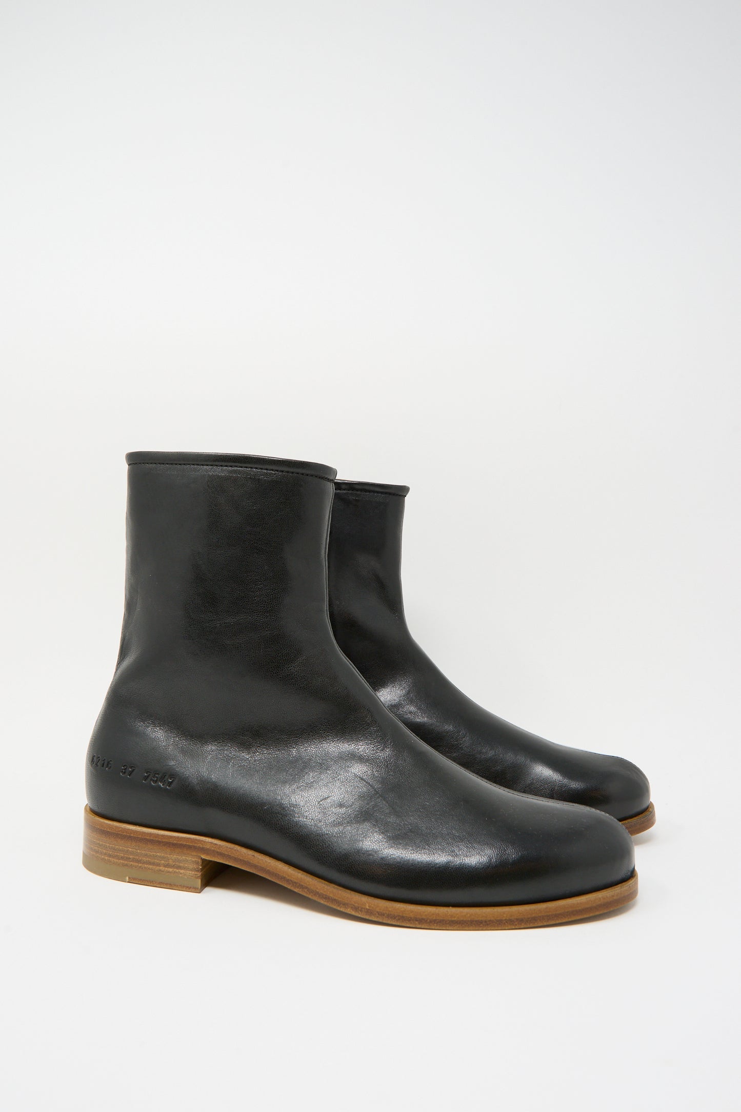 The Common Projects Zipper Boot Article 6216 in Black features smooth black leather, light brown wooden soles, crafted in Italy, and is shown against a plain white background.
