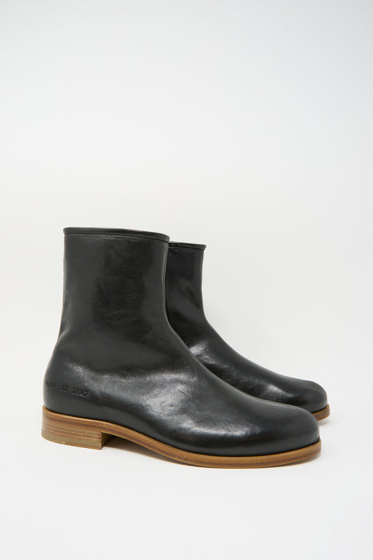 The Common Projects Zipper Boot Article 6216 in Black features smooth black leather, light brown wooden soles, crafted in Italy, and is shown against a plain white background.