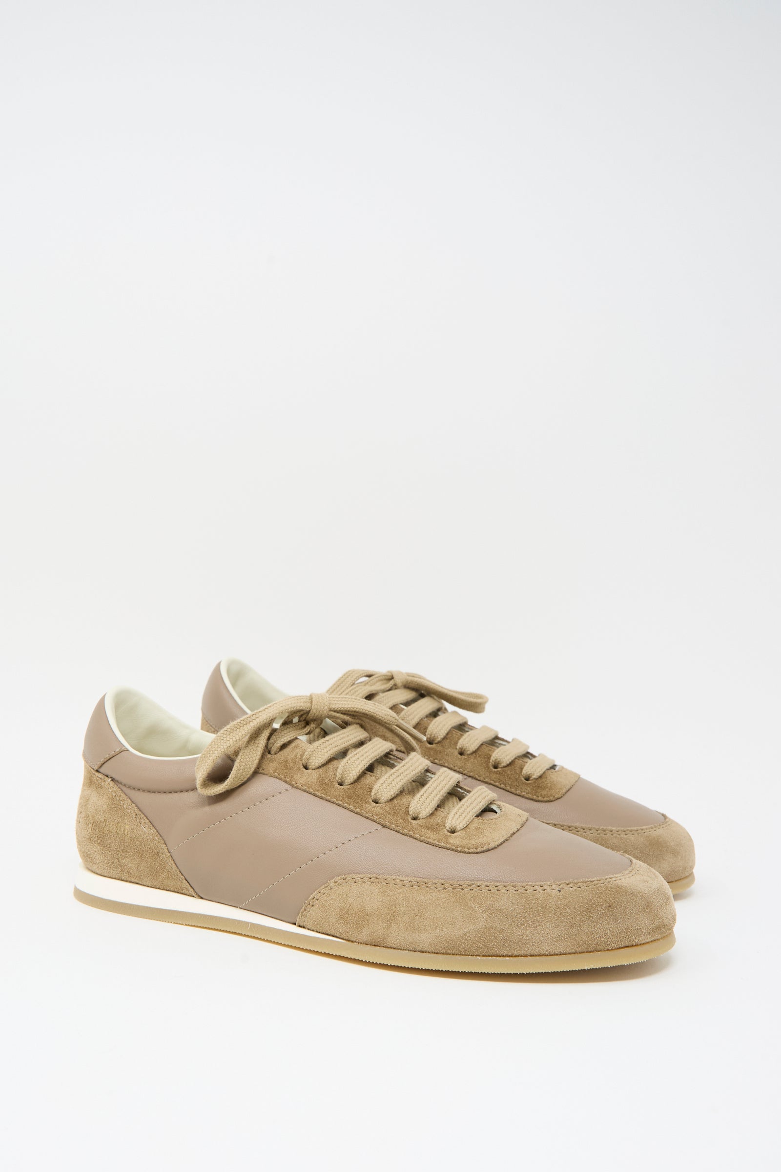 The Common Projects Minimal Runner Article 4182 in Taupe is a pair of low-top sneakers crafted in Italy with tan and beige calfskin suede and leather panels, white midsoles, and tan laces, shown against a white background.