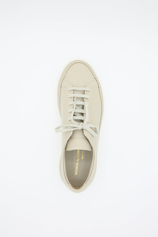 A single luxury footwear brand, Common Projects Original Achilles Low 3701 sneaker with laces in Taupe on a white background, Made in Italy.