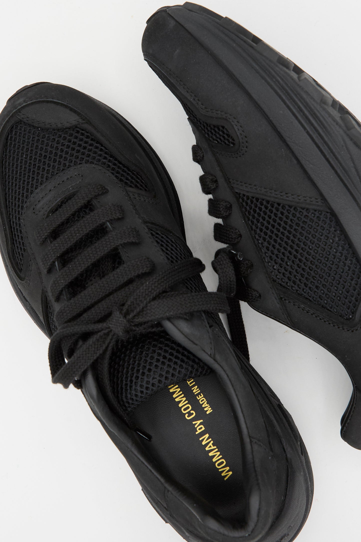 The Premium Mesh Runner in Black by Common Projects features mesh panels, thick soles, and "Woman by Common Projects" text on the insole. Made in Italy, these sneakers combine retro style with modern design.