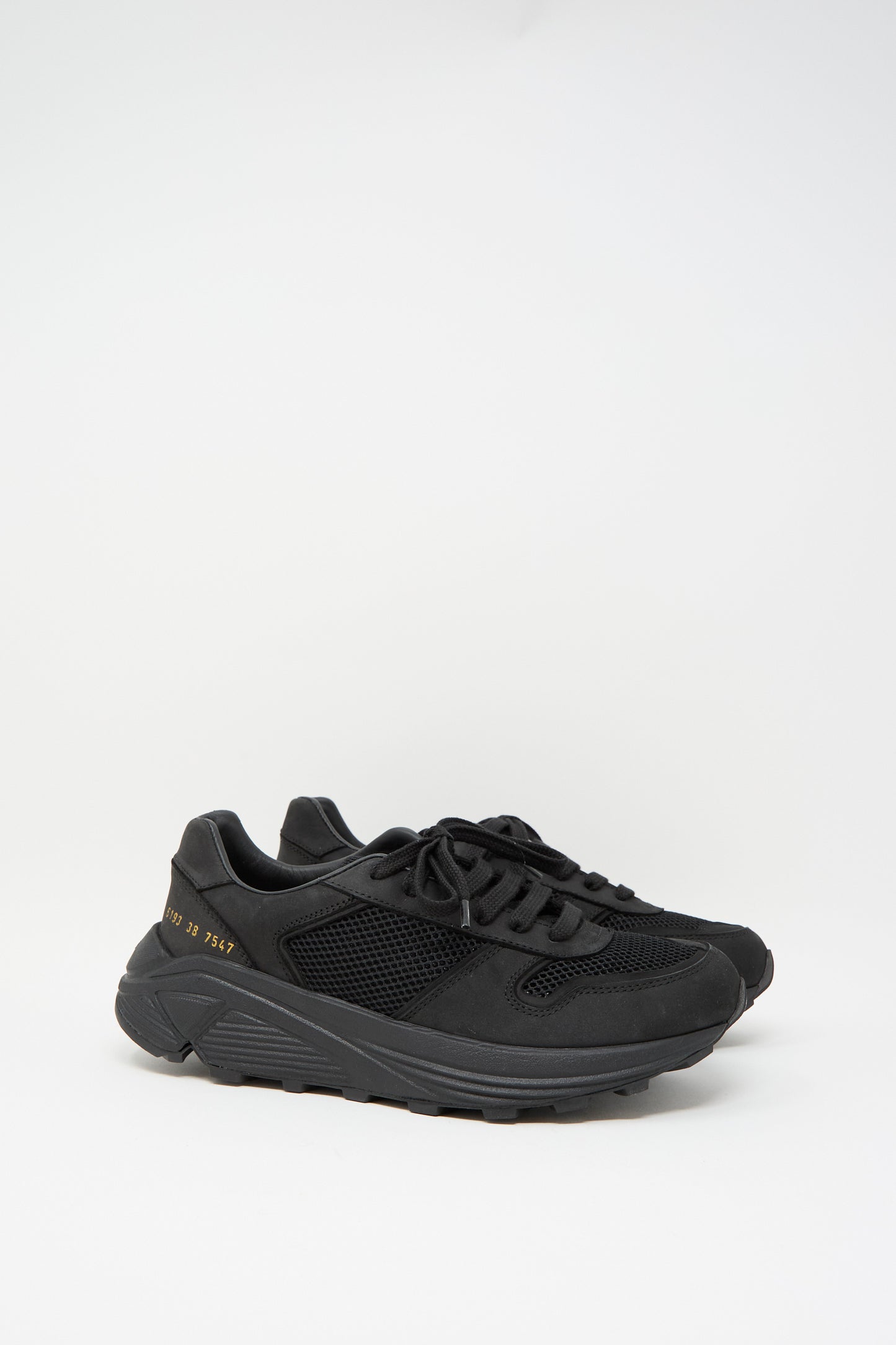 The Premium Mesh Runner in Black by Common Projects is a retro style sneaker made from nappa leather, showcasing mesh panels and a thick sole with gold numbers on the side, set against a plain white background.