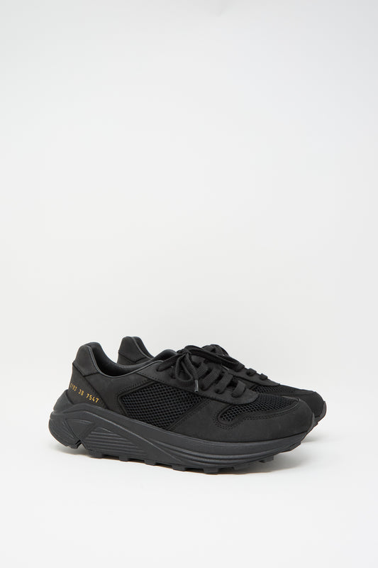 The Premium Mesh Runner in Black by Common Projects is a retro style sneaker made from nappa leather, showcasing mesh panels and a thick sole with gold numbers on the side, set against a plain white background.