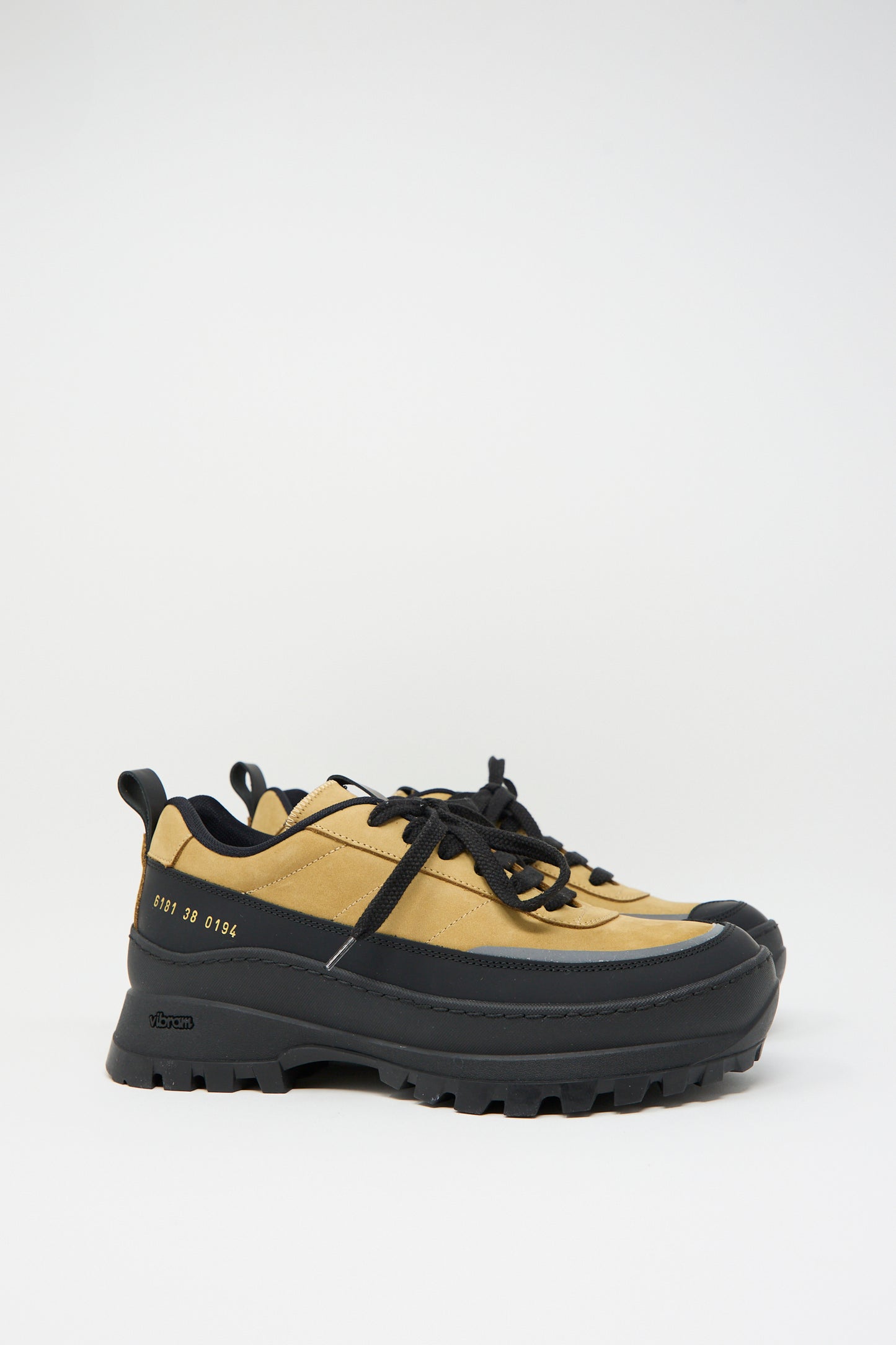 A pair of Common Projects Track Hiker Article 6181 in Ocra, featuring yellow and black lace-up design with thick, rugged Vibram soles, placed against a plain white background.