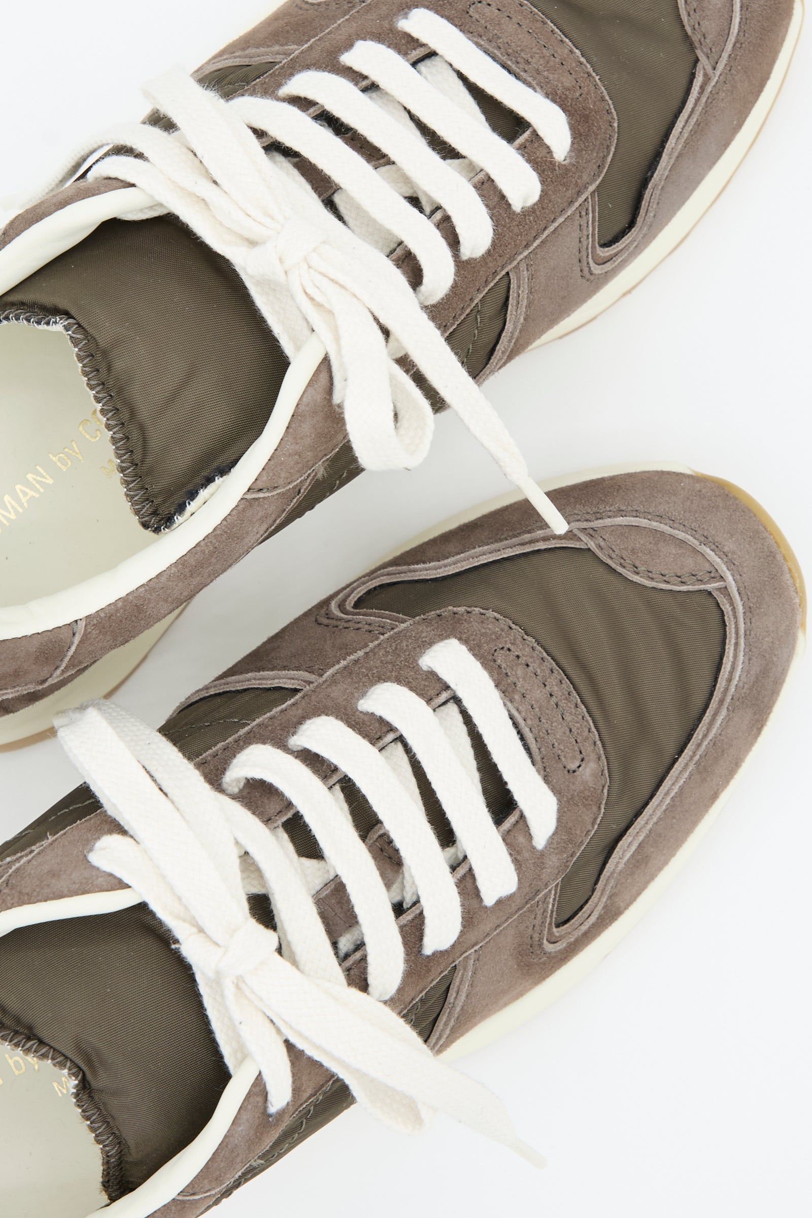 Close-up of the Common Projects Track Premium Article 6171 sneakers in Coffee, showcasing their brown suede and nylon upper, white laces, and cushioned footbed, displayed against a white background.