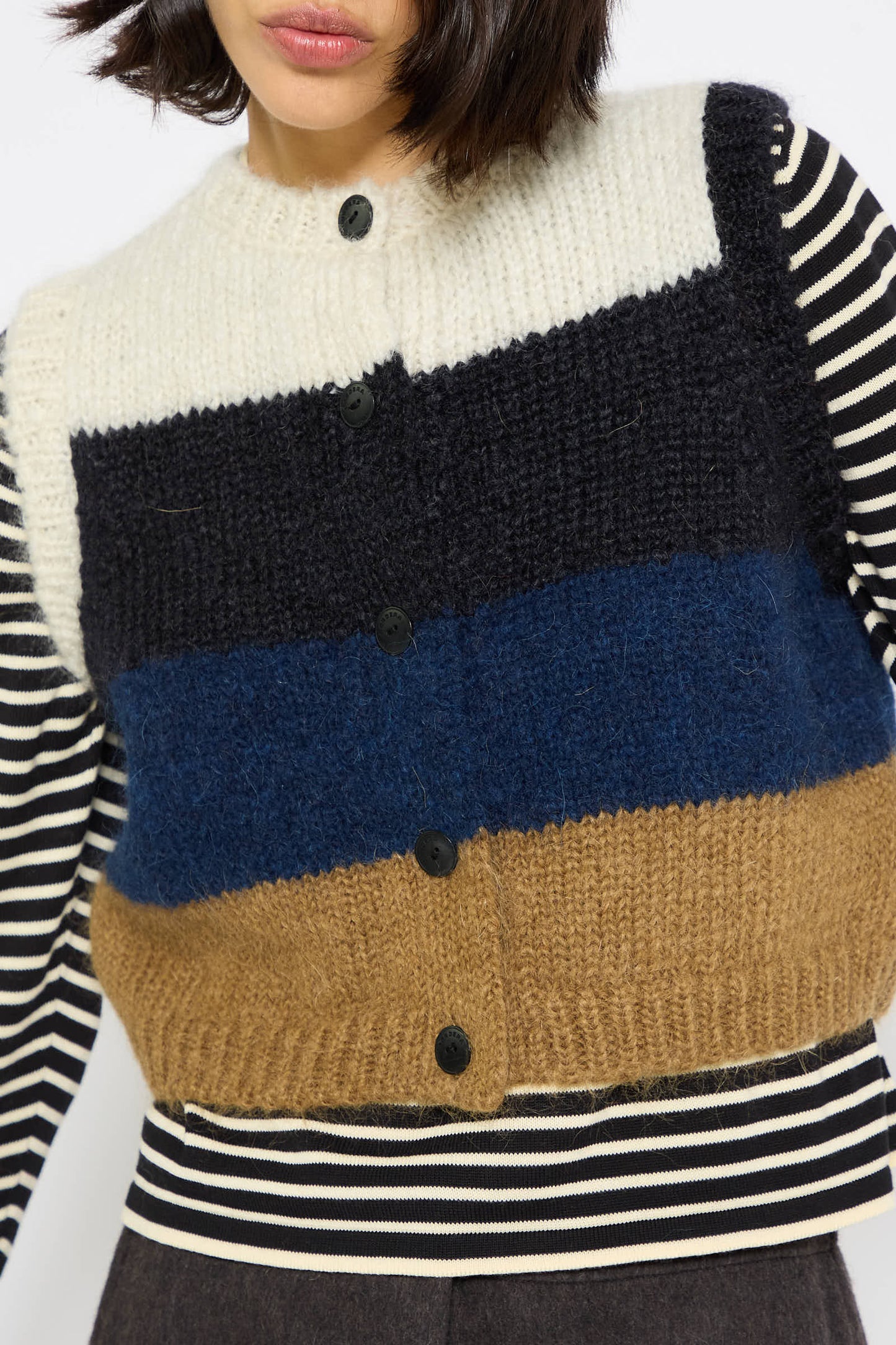 A person wearing a color-blocked, wool-knit cardigan with black buttons over a Cordera Alpaca and Mohair Waistcoat in Striped.