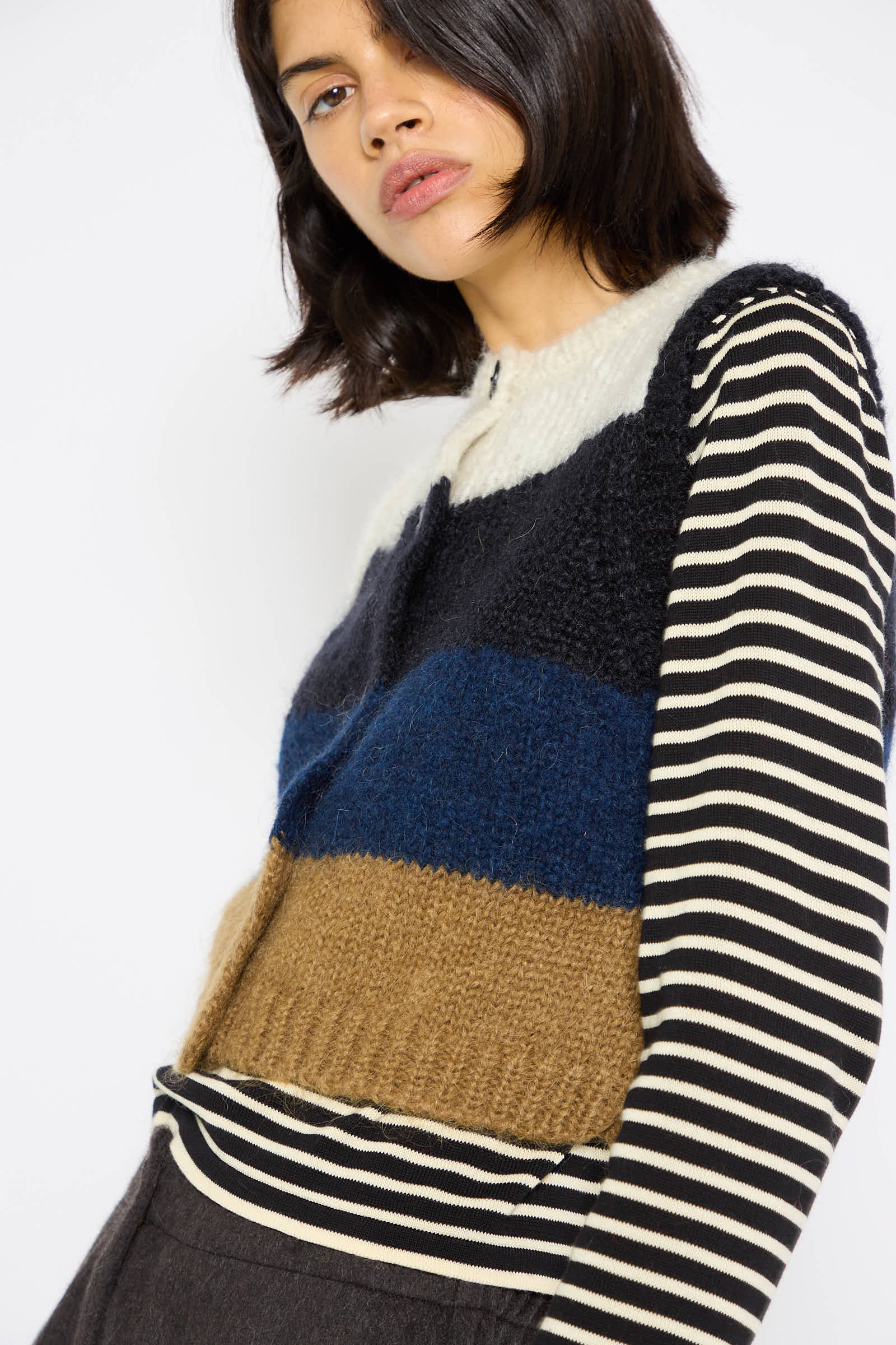 A woman with shoulder-length dark hair is wearing the Cordera Alpaca and Mohair Waistcoat in Striped, layered over an ethical black and white long-sleeve shirt. She is gazing slightly off-camera.