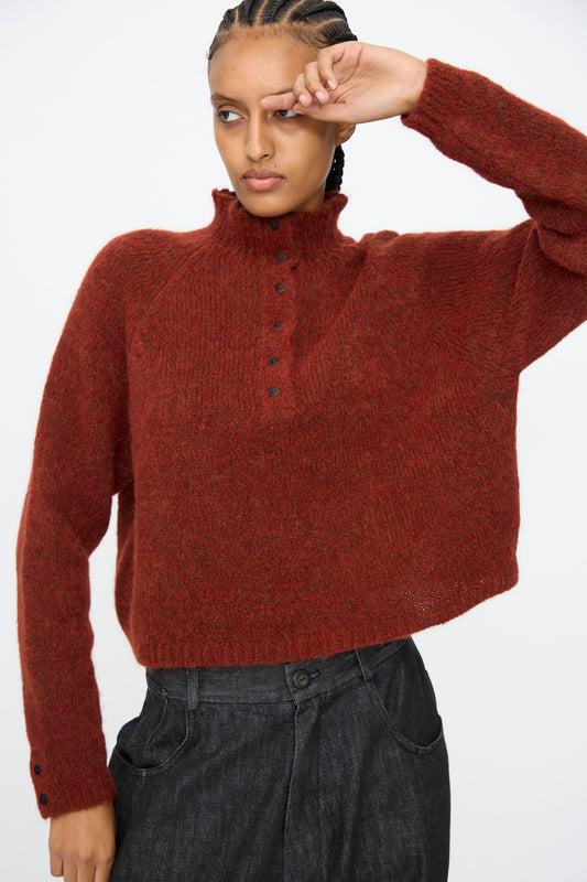 A person models the Cordera Baby Alpaca Polo Sweater in Terracotta, featuring black buttons, paired with dark high-waisted pants against a plain white background.