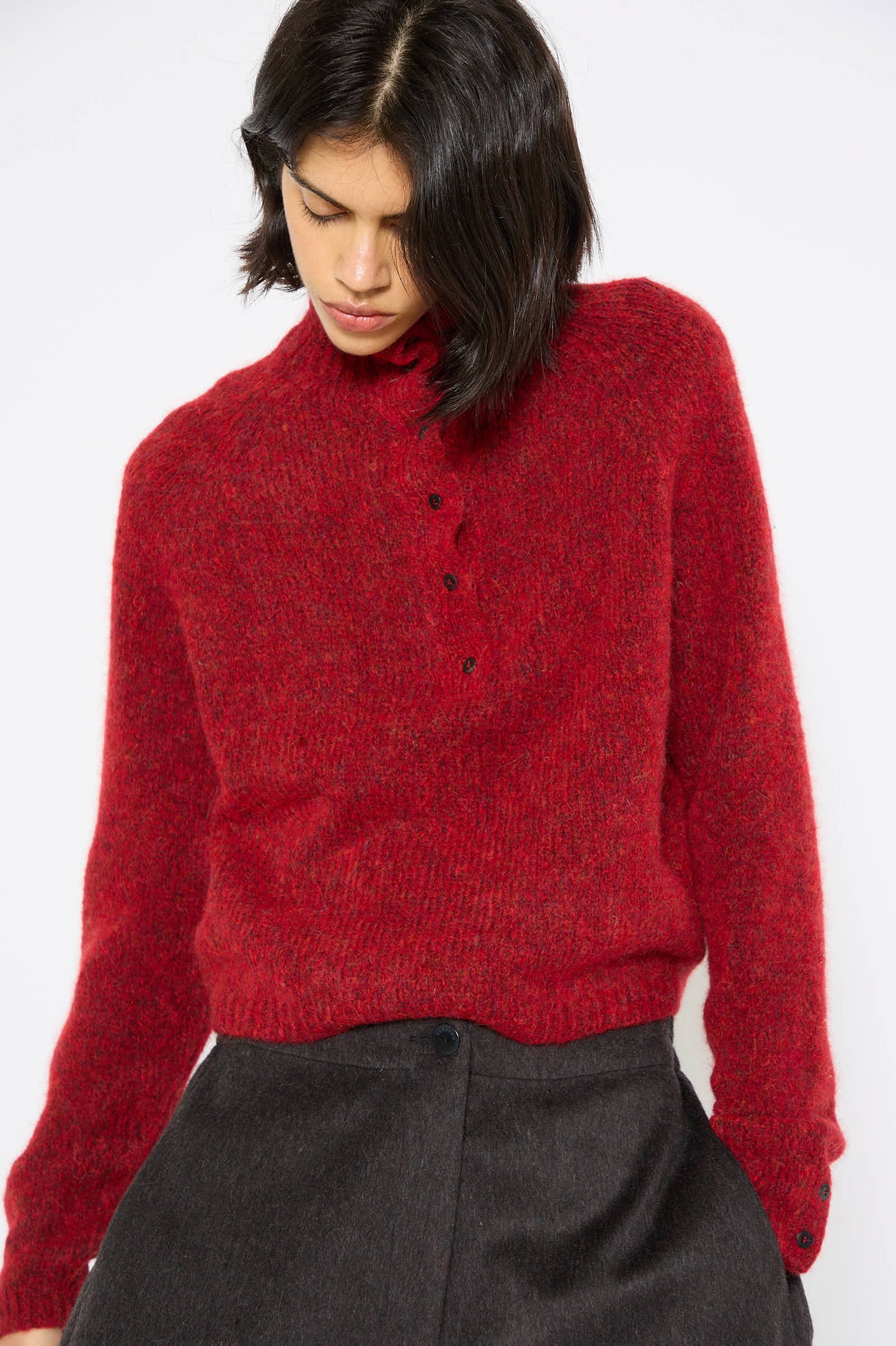 Person wearing the Baby Alpaca Polo Sweater in Dahlia by Cordera, paired with dark pants and looking down. The background is plain and white.