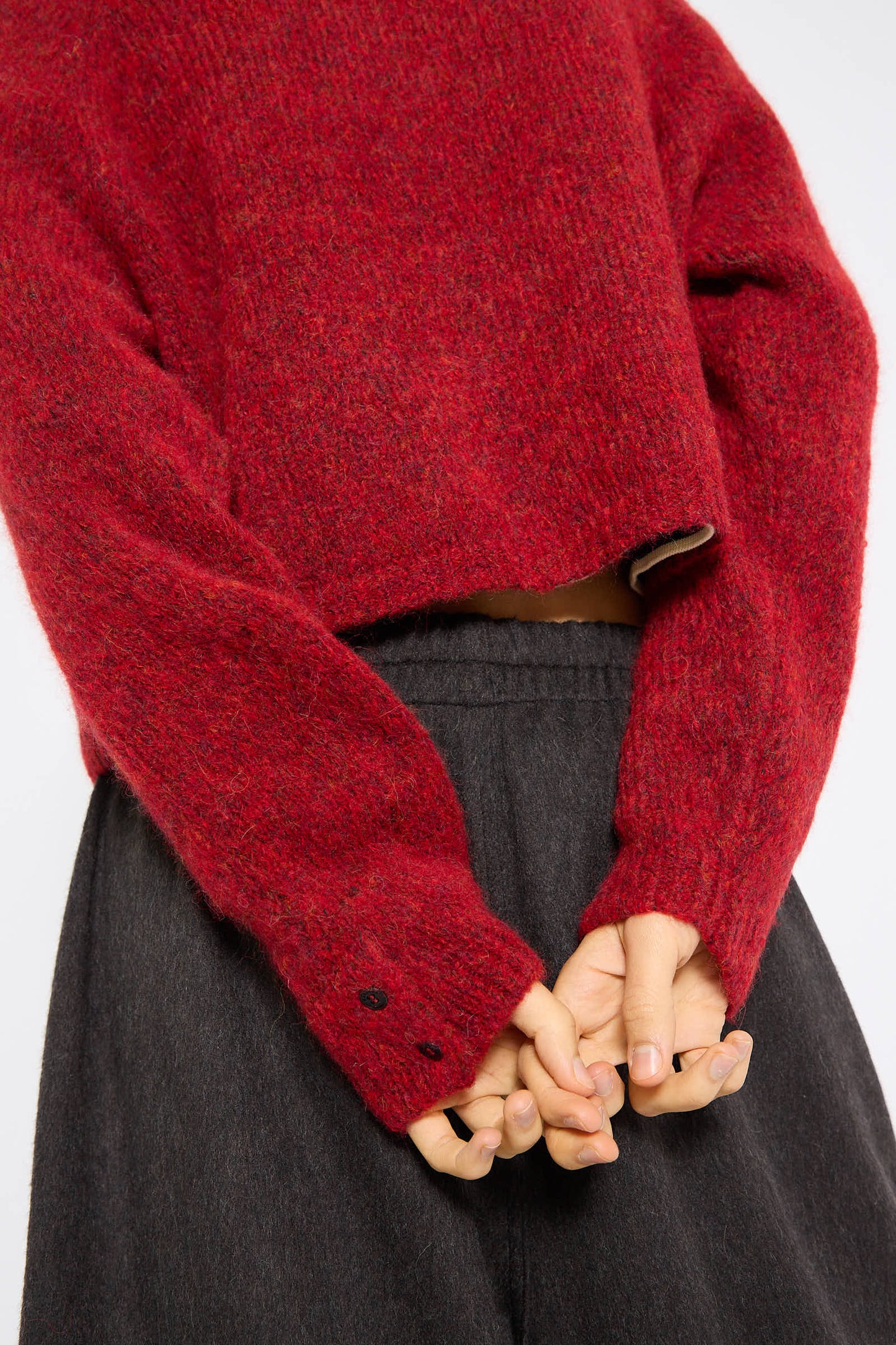 Person wearing the Baby Alpaca Polo Sweater in Dahlia by Cordera, with sleeves pulled down, hands clasped behind their back, and a dark skirt.