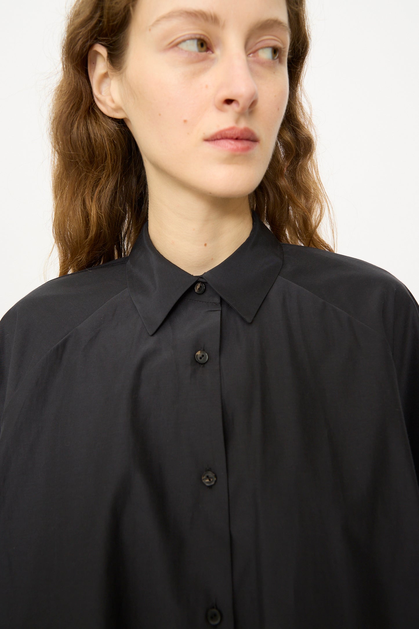 A person with wavy brown hair wears the Cordera Balloon Shirt in Black, gazing slightly to the side against a plain background.
