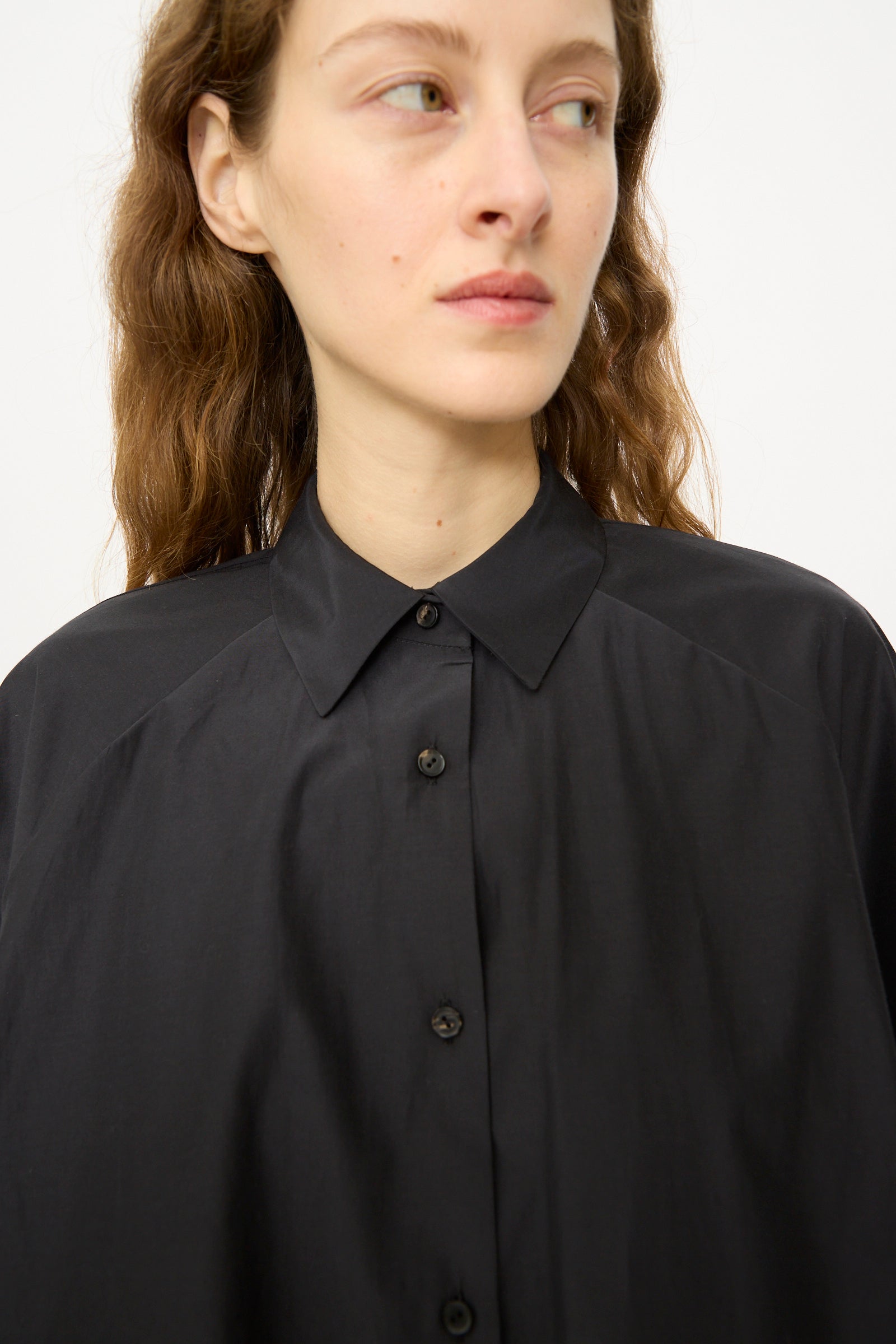 A person with wavy brown hair wears the Cordera Balloon Shirt in Black, gazing slightly to the side against a plain background.