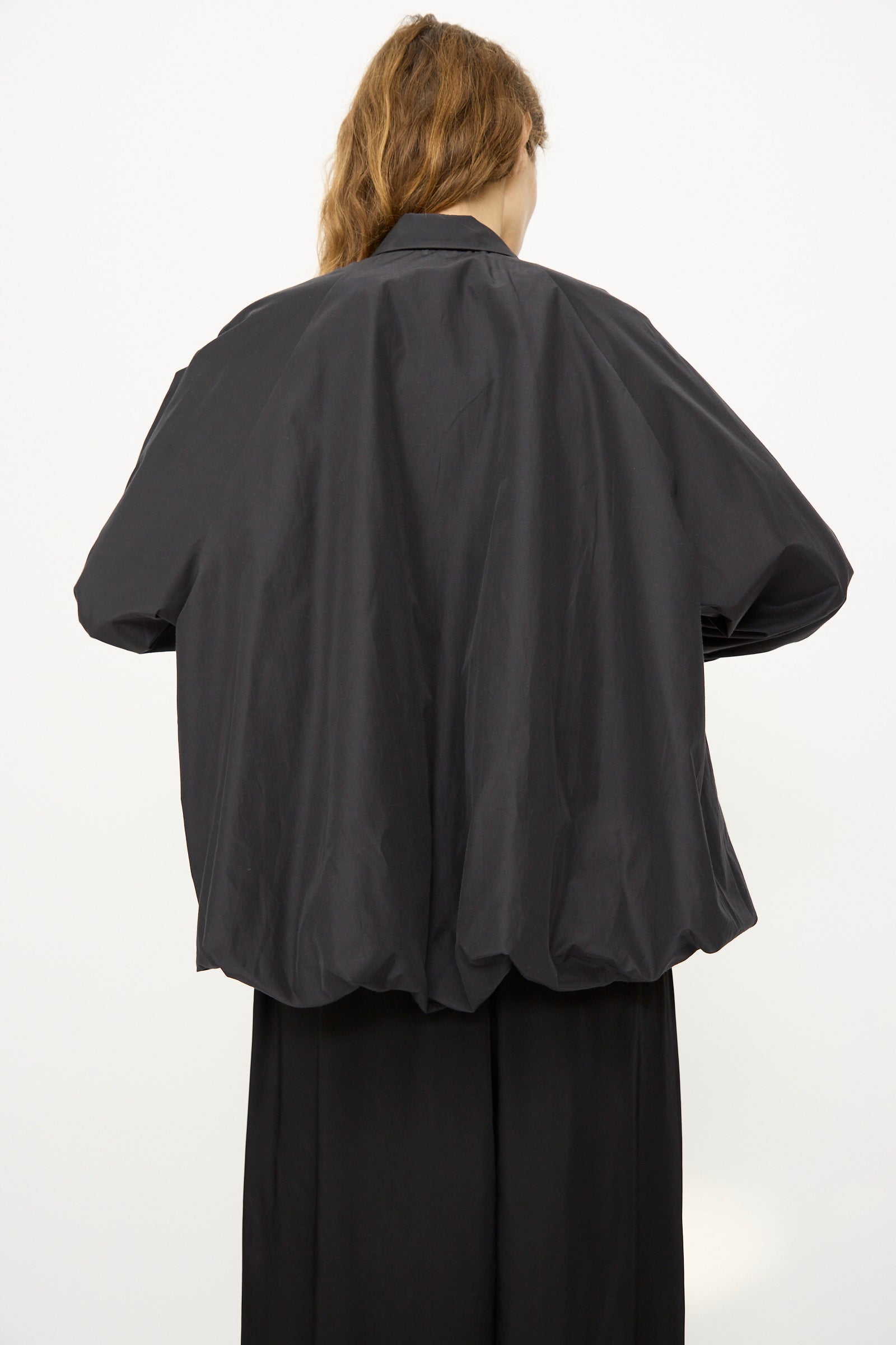 Model with long, light brown hair shown from the back wearing Cordera's Balloon Shirt in Black with voluminous sheer sleeves and black pants, set against a plain white background.