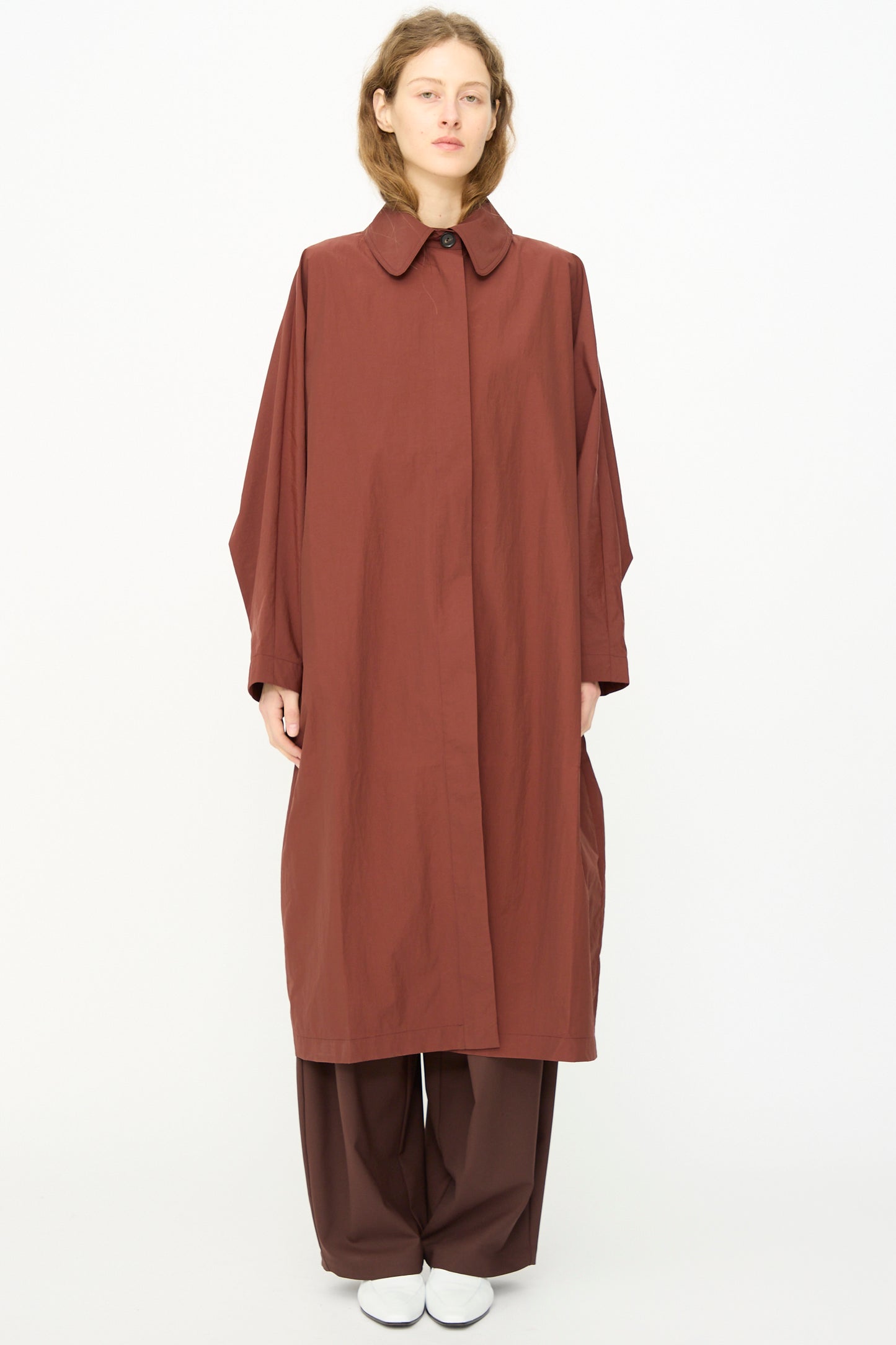 A model faces forward in the Cordera Batwing Trench in Sienna, styled with matching wide-leg pants and white shoes, set against a plain white background.