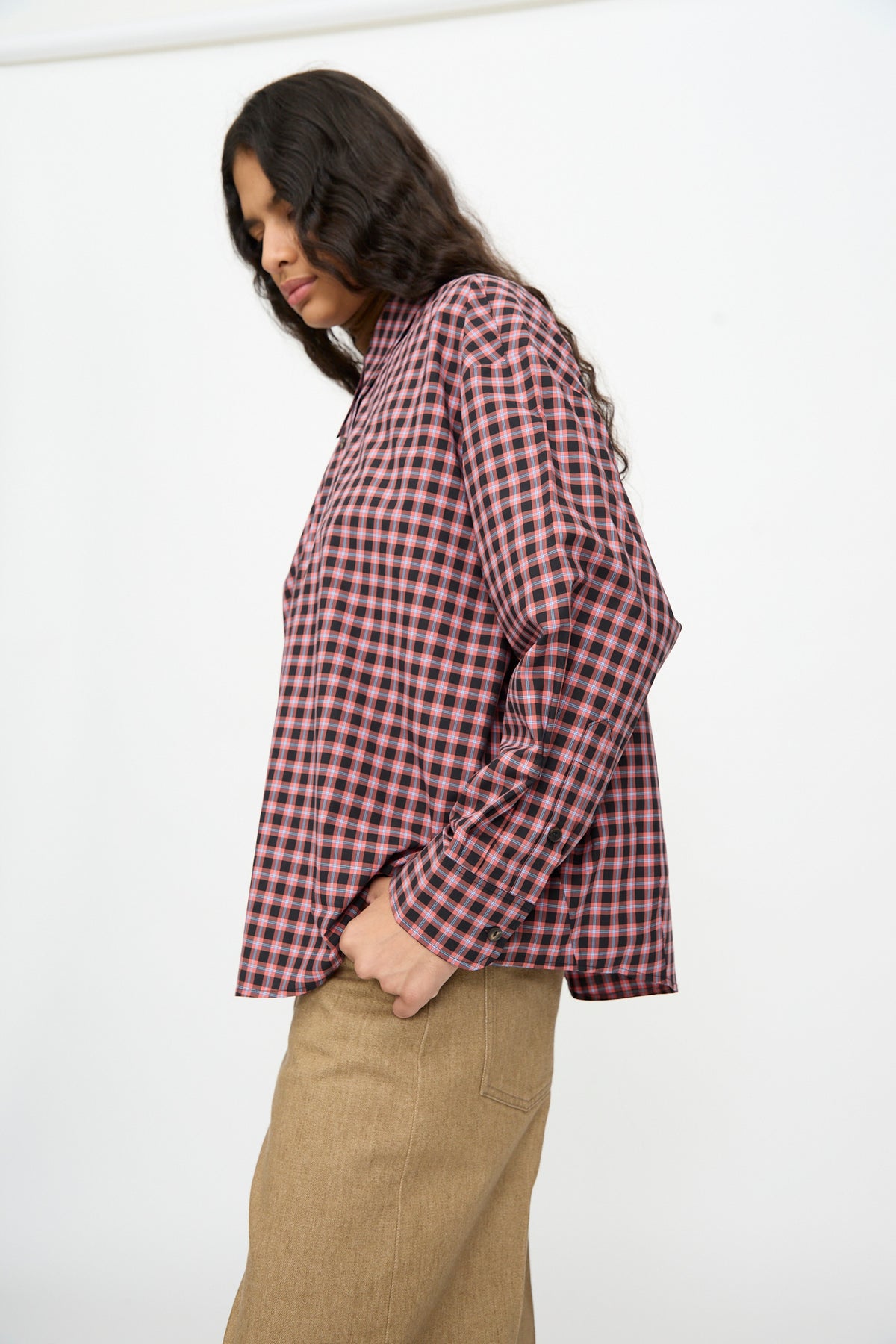 Person wearing a Cordera Checked Oversized Shirt in Orange and Black, an oversized, long-sleeved cotton top with an Italian collar and a hand in their pocket.