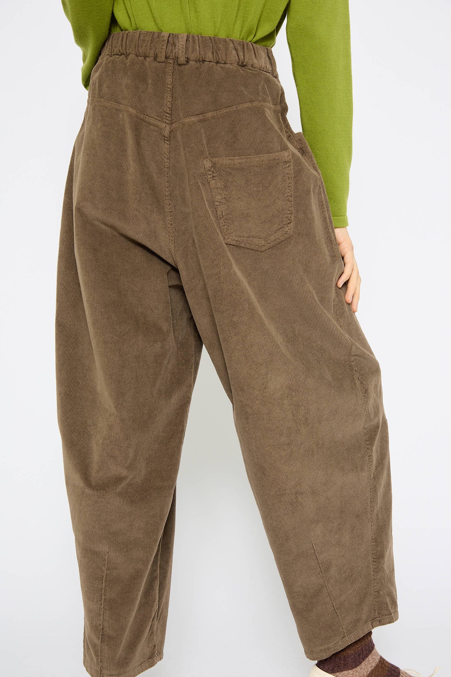 A person wearing Cordera’s Corduroy Baggy Pant in Moss with an elastic waistband and a green shirt, standing with their back to the camera.