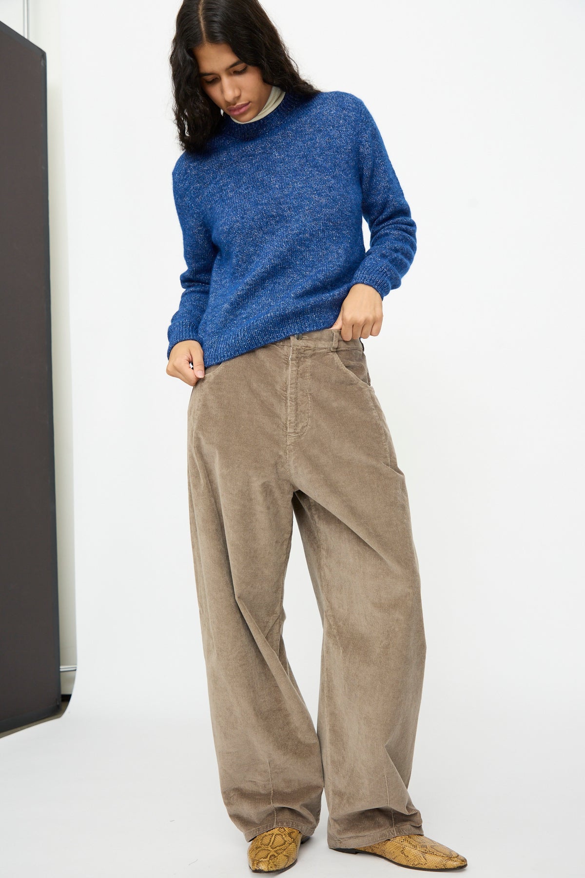A person wearing a blue sweater and Cordera Corduroy Baggy Pants in Sage, featuring a relaxed, wide-leg fit.