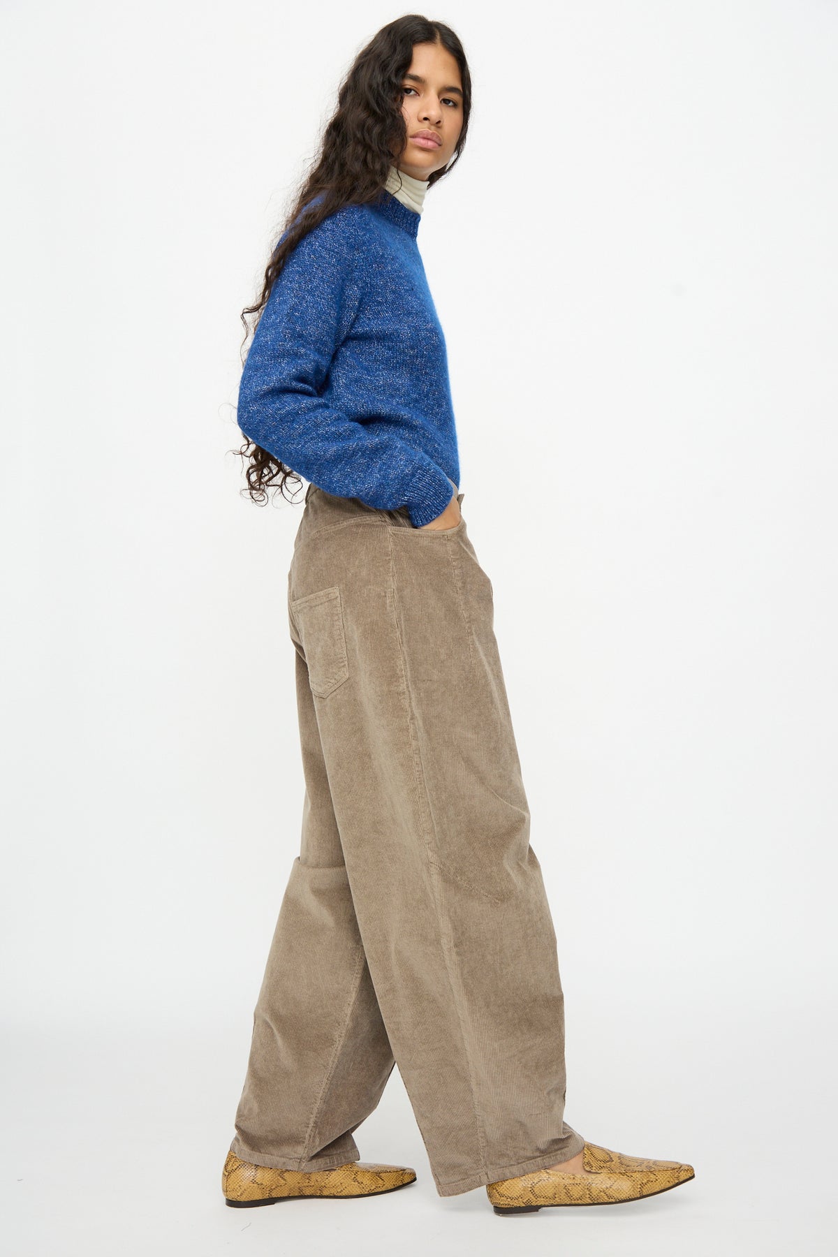 A person wearing a blue sweater and Cordera Corduroy Baggy Pants in Sage, featuring a relaxed, wide-leg fit.