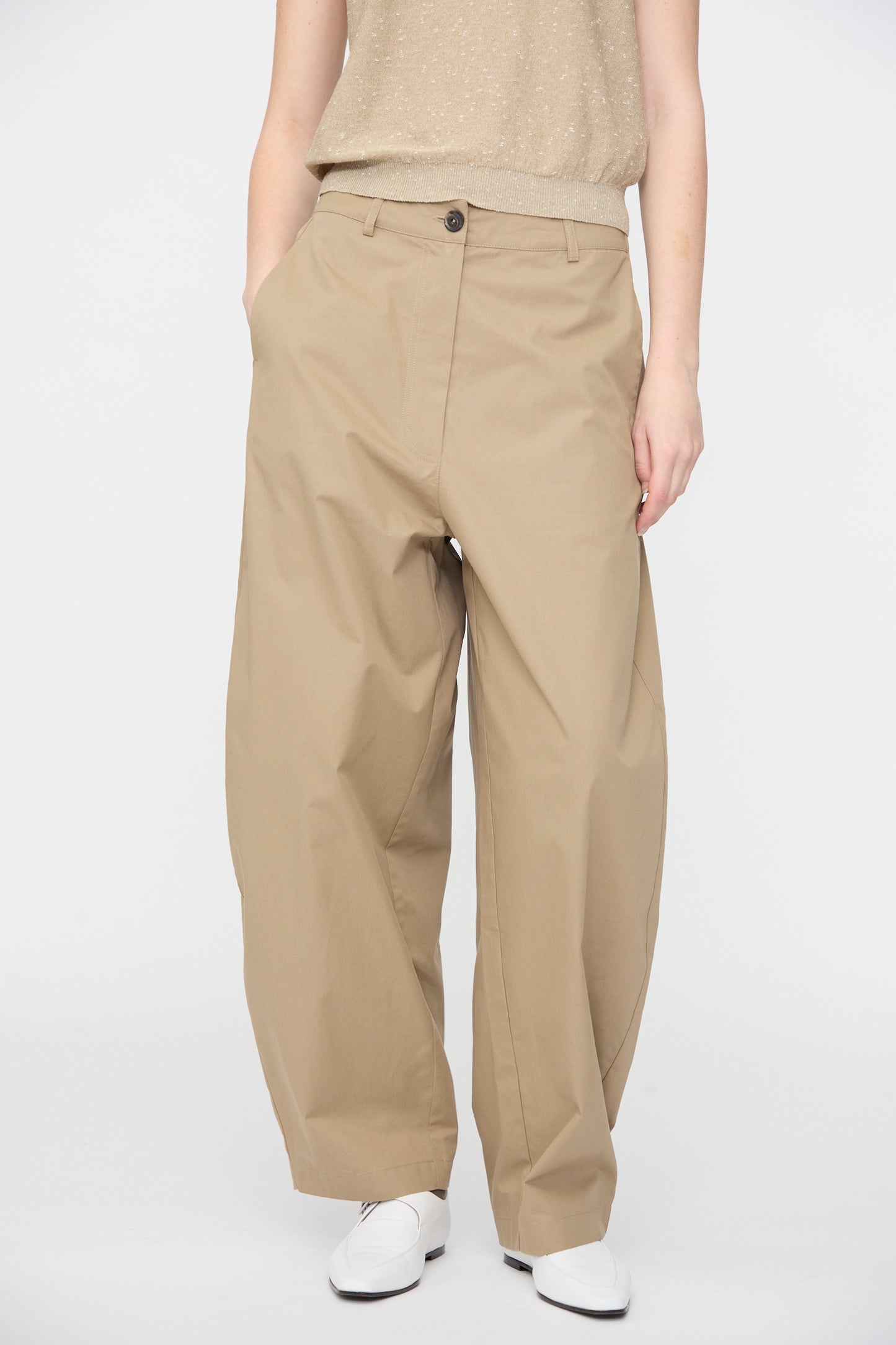 A person models Cordera's Cotton Curved Pants in Camel with a beige sleeveless top and white shoes, standing against a plain white background.