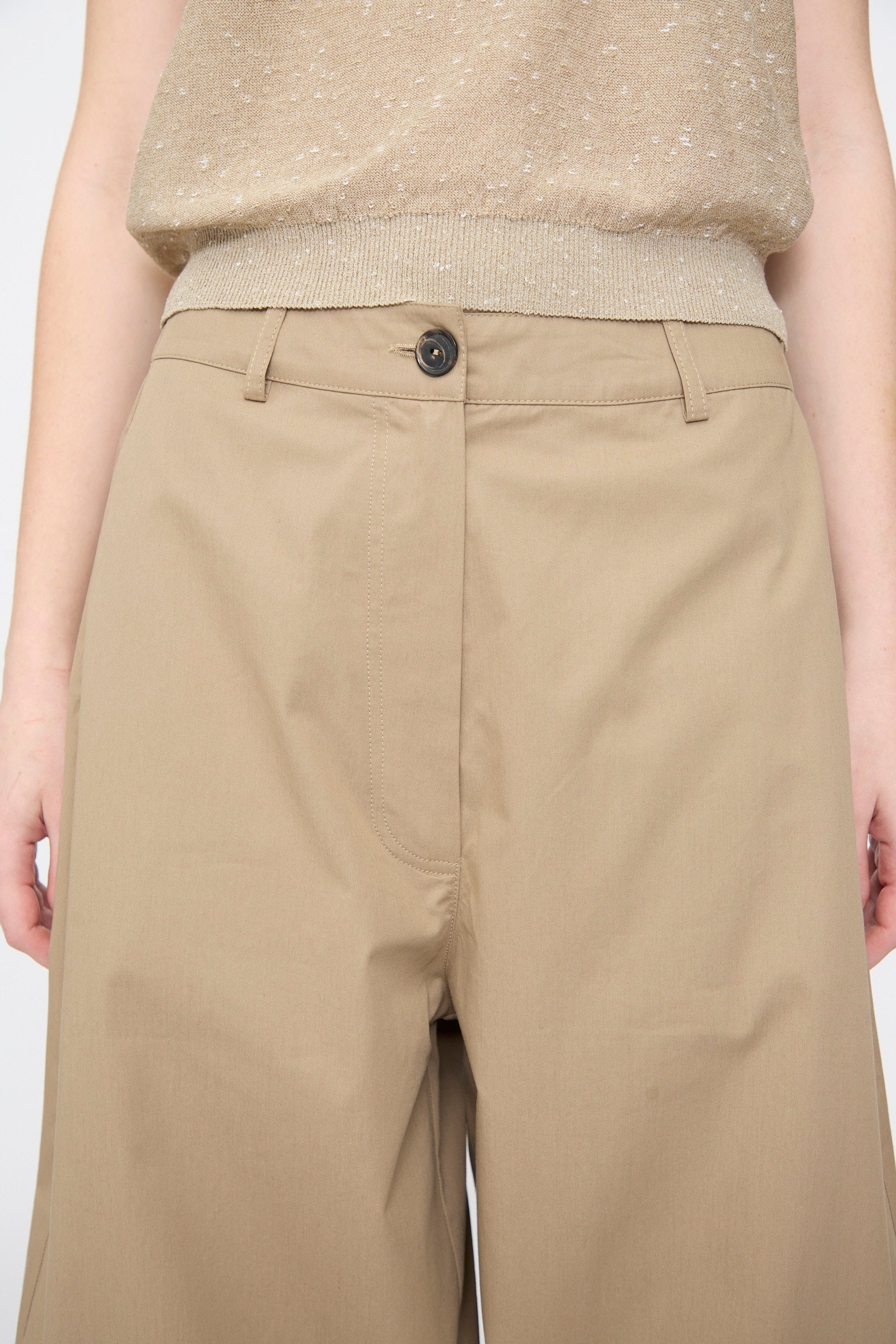 A person wearing Cordera’s Cotton Curved Pants in Camel, shown from waist to mid-thigh, paired with a light brown sleeveless top.