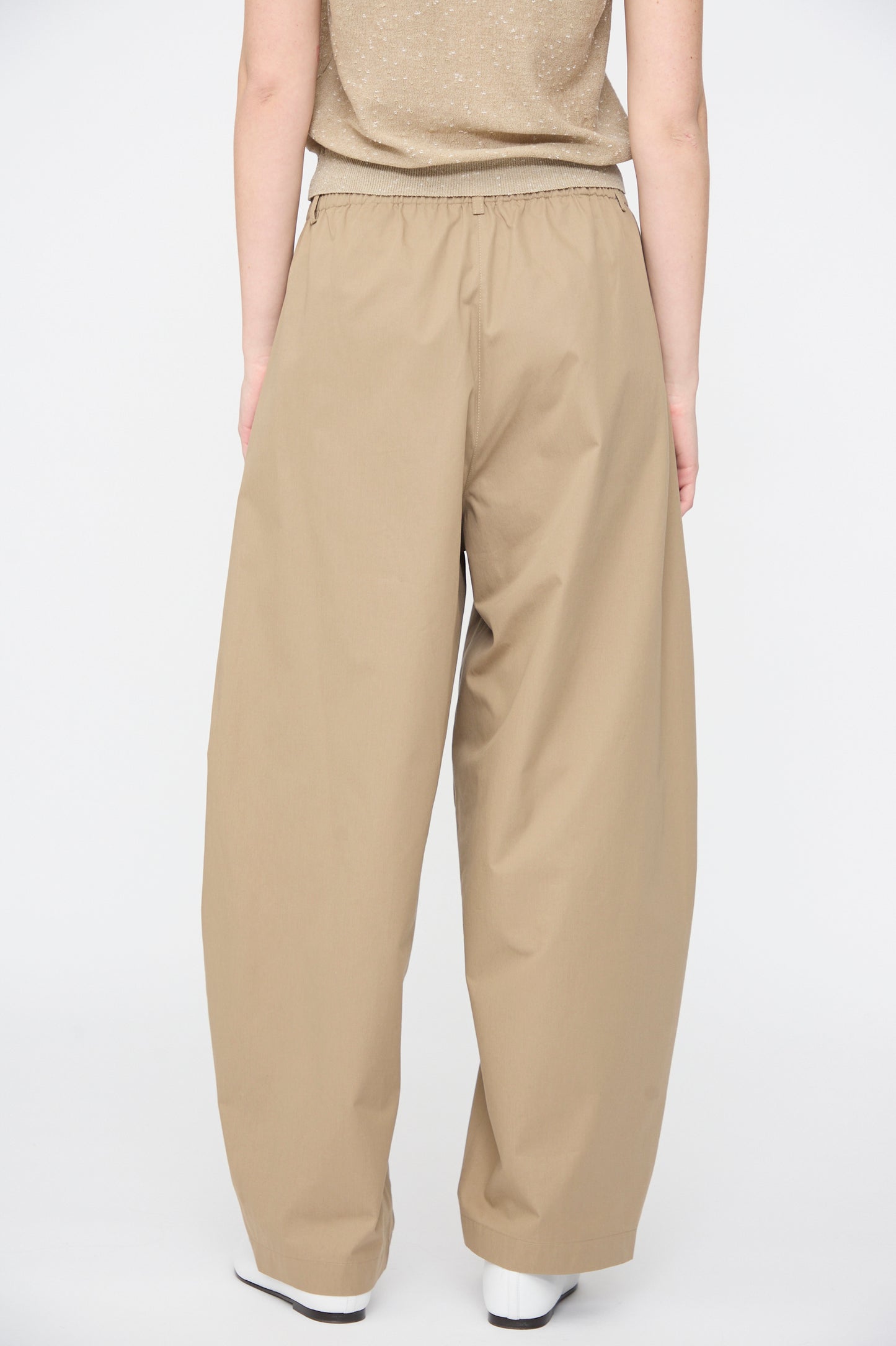 A person wearing Cordera's Cotton Curved Pants in Camel and a beige shirt stands with their back to the camera against a plain white background.