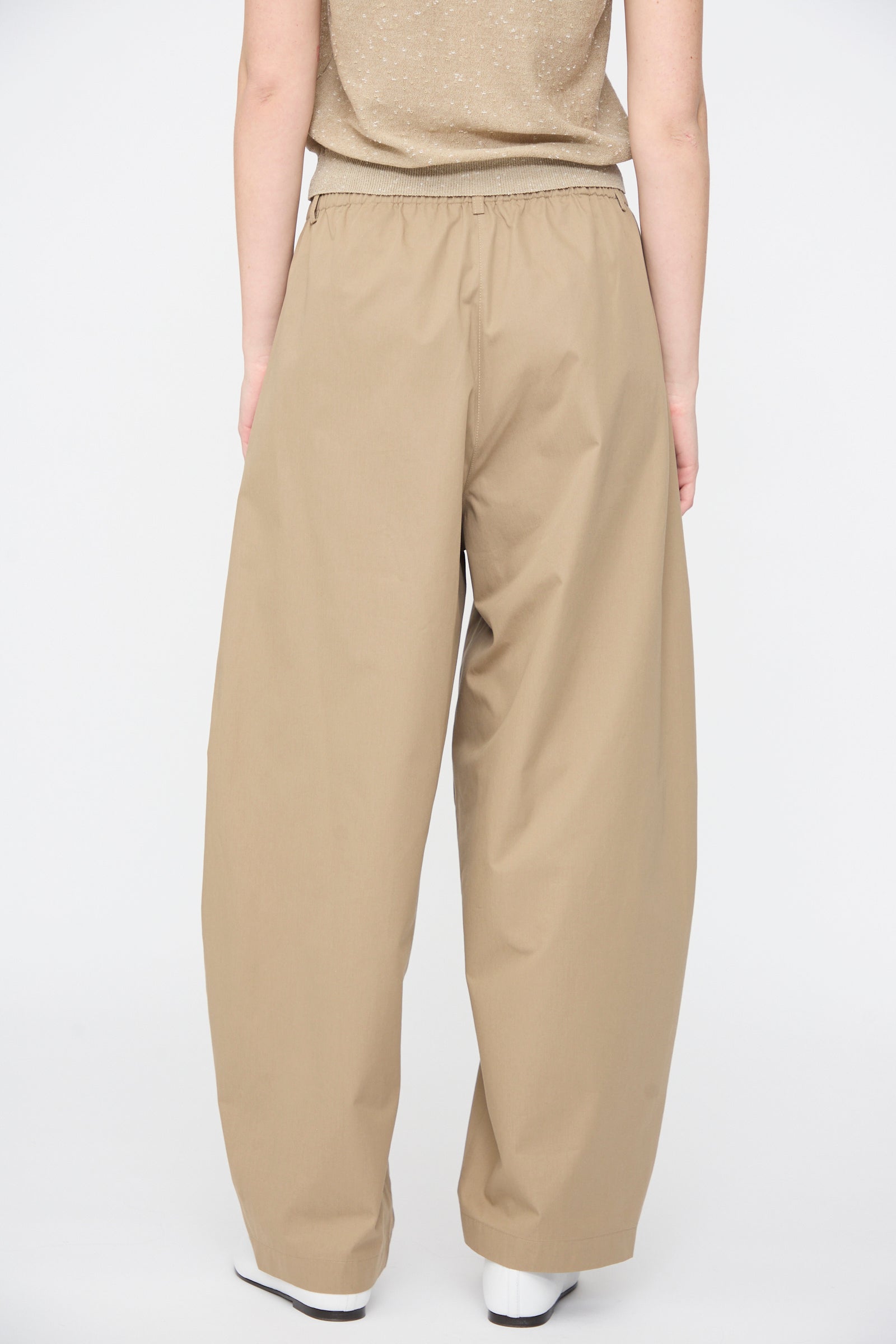 A person wearing Cordera's Cotton Curved Pants in Camel and a beige shirt stands with their back to the camera against a plain white background.