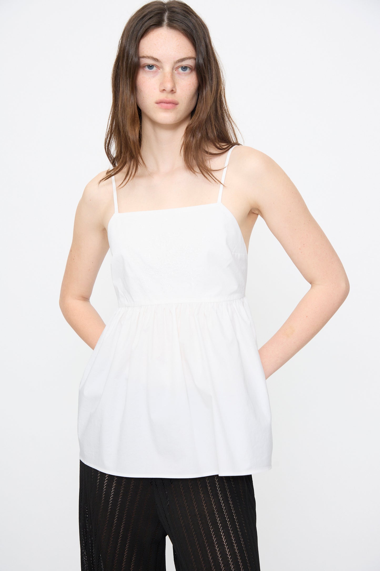 A person wears the Cordera Cotton Embroidered Top in White with an adjustable back tie and black textured pants, standing against a plain white background.