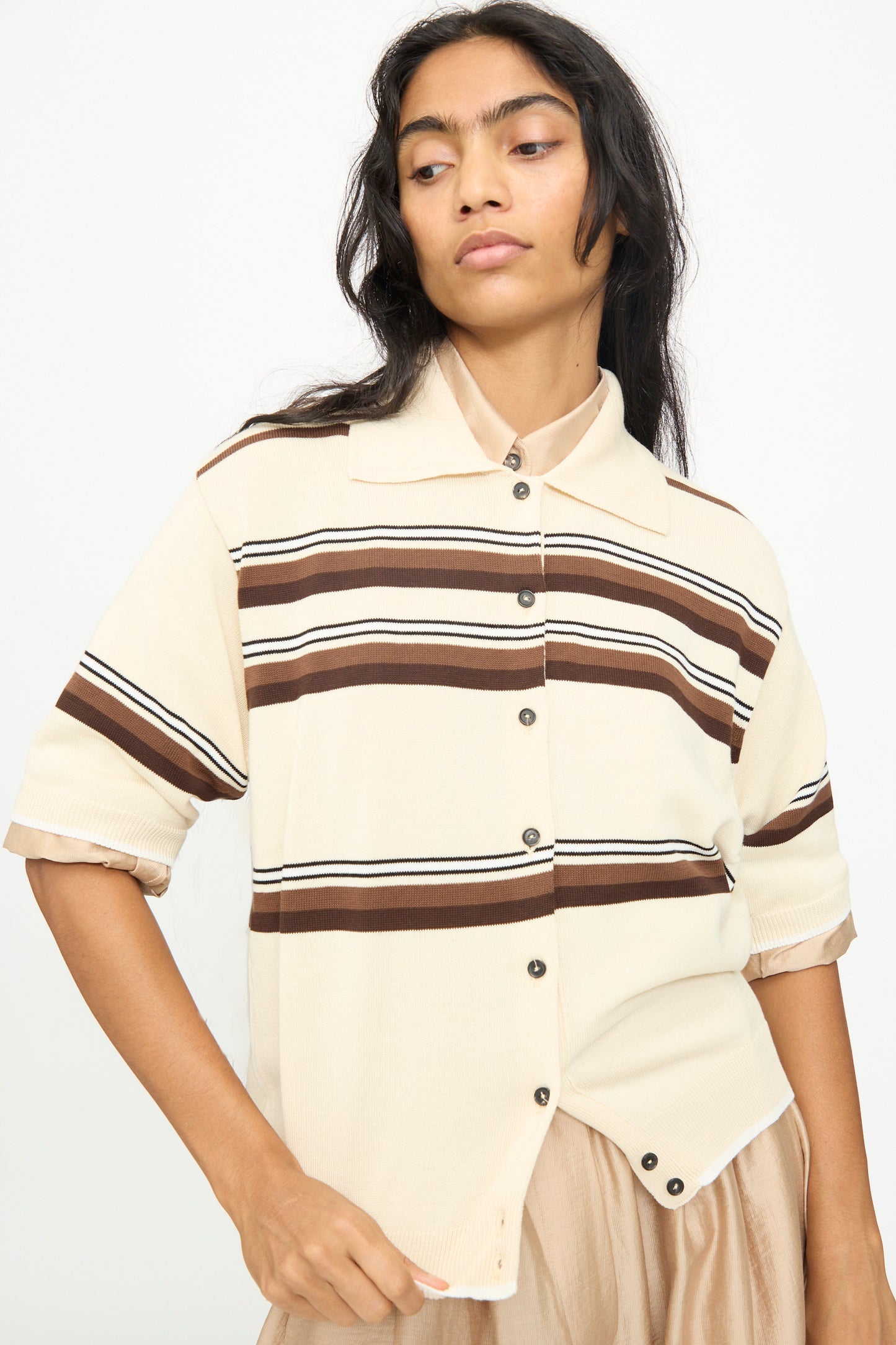 A person is wearing the Cordera Cotton Polo in Striped, a beige short-sleeve cotton shirt featuring brown horizontal stripes and a polo collar, standing against a plain background.