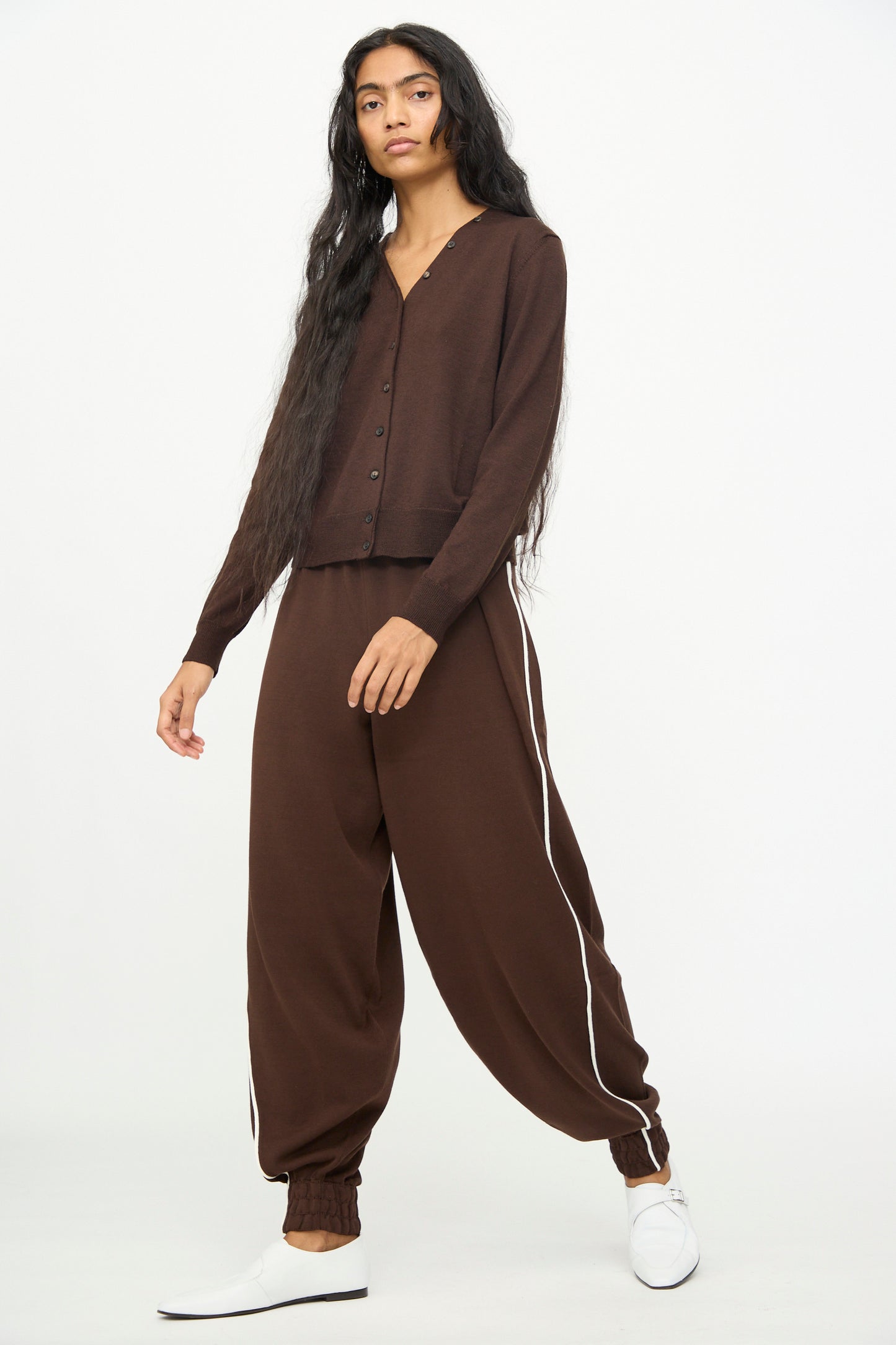 A person is wearing Cordera’s Cotton Sporty Pants in Brown, featuring white side stripes and an elastic waistband, paired with a matching brown button-up cardigan and white shoes, standing against a plain white background.