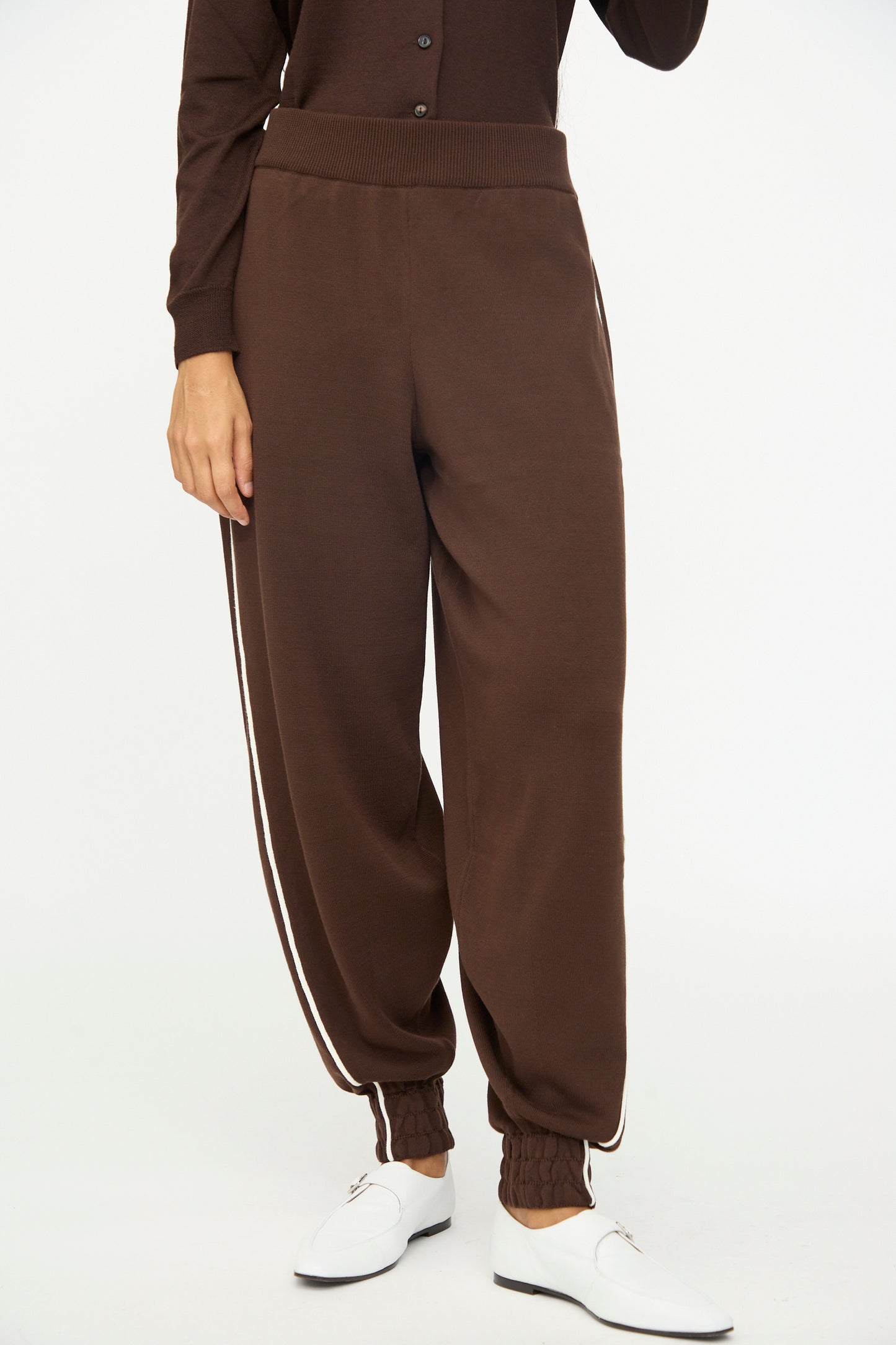 A person is seen wearing the Cordera Cotton Sporty Pants in Brown, jogger-style cotton pants with a white side stripe and an elastic waistband, paired with white shoes and standing against a plain white background.