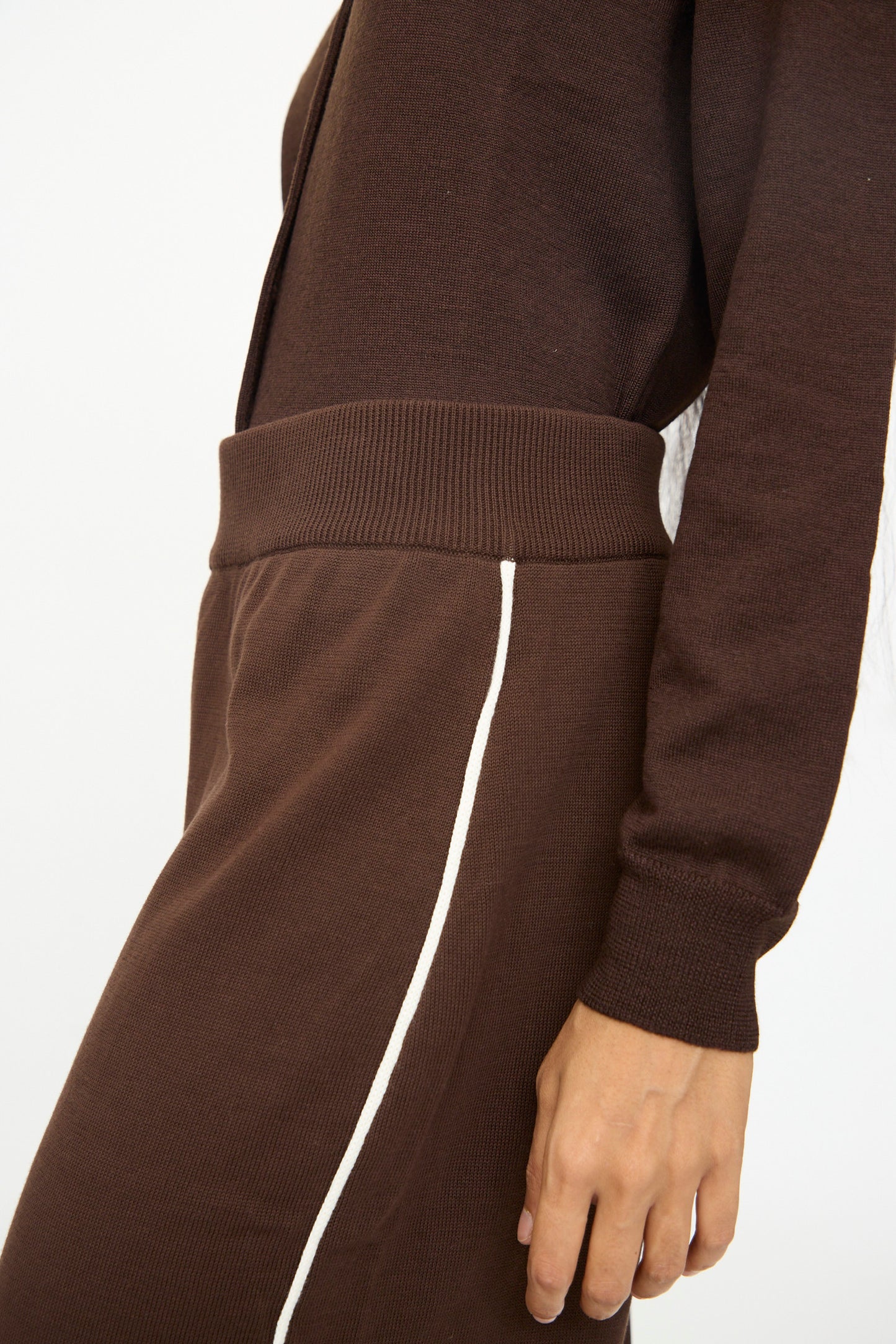 A person wearing Cordera's Cotton Sporty Pants in Brown, featuring a white side stripe and elastic waistband, paired with a brown long-sleeve top, shown from shoulder to knee.