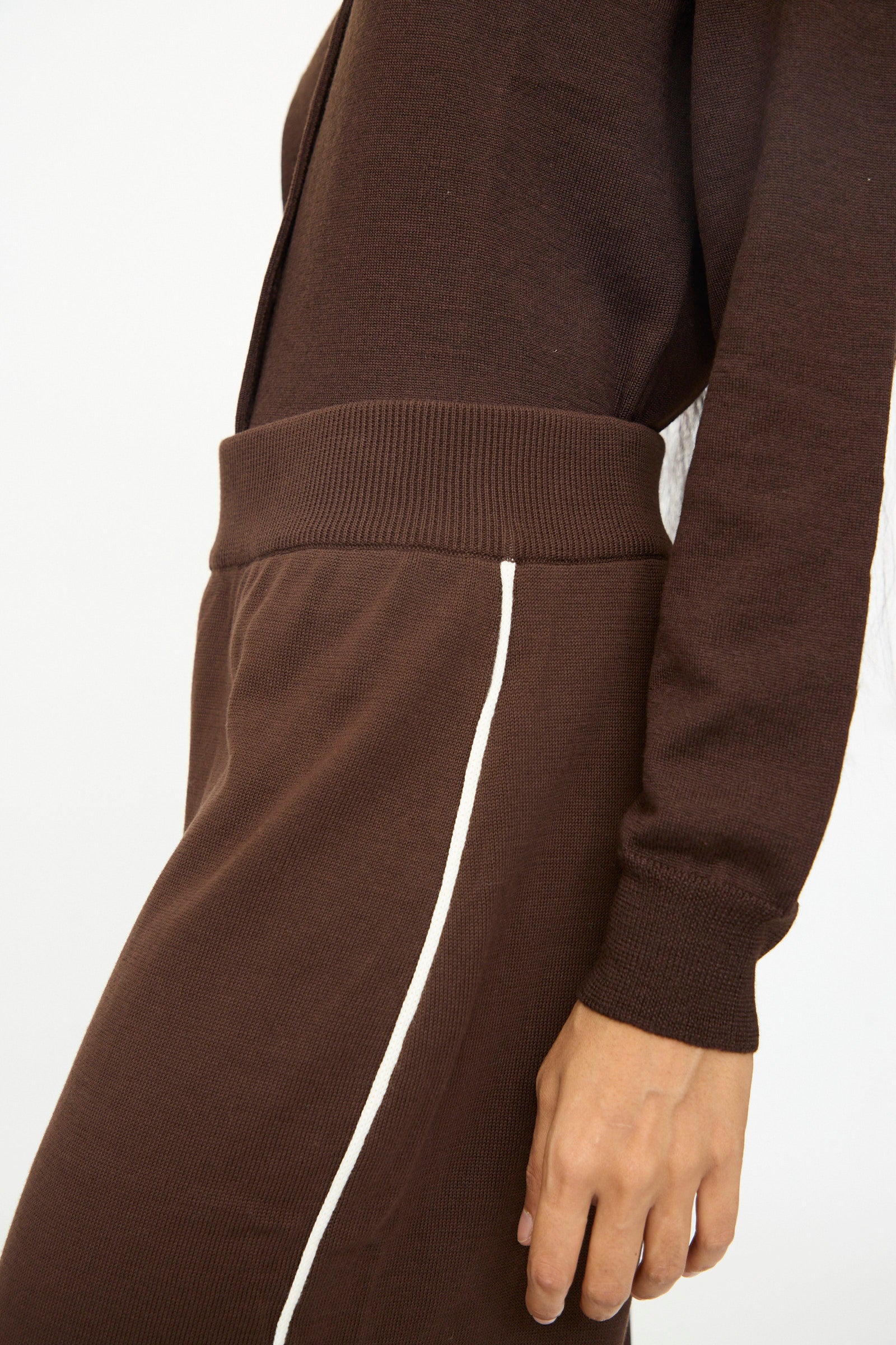 A person wearing Cordera's Cotton Sporty Pants in Brown, featuring a white side stripe and elastic waistband, paired with a brown long-sleeve top, shown from shoulder to knee.