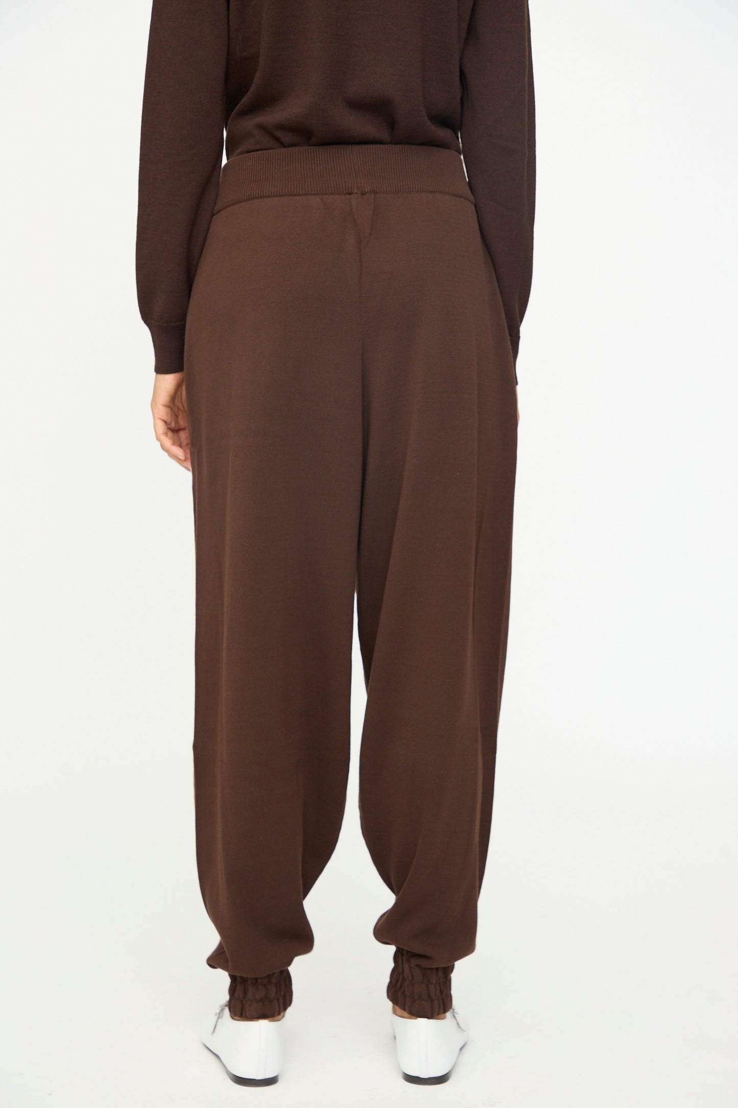 A person is seen from the back wearing Cordera’s Cotton Sporty Pants in Brown—loose-fitting cotton pants with an elastic waistband—paired with a matching brown top and white shoes, standing against a white background.