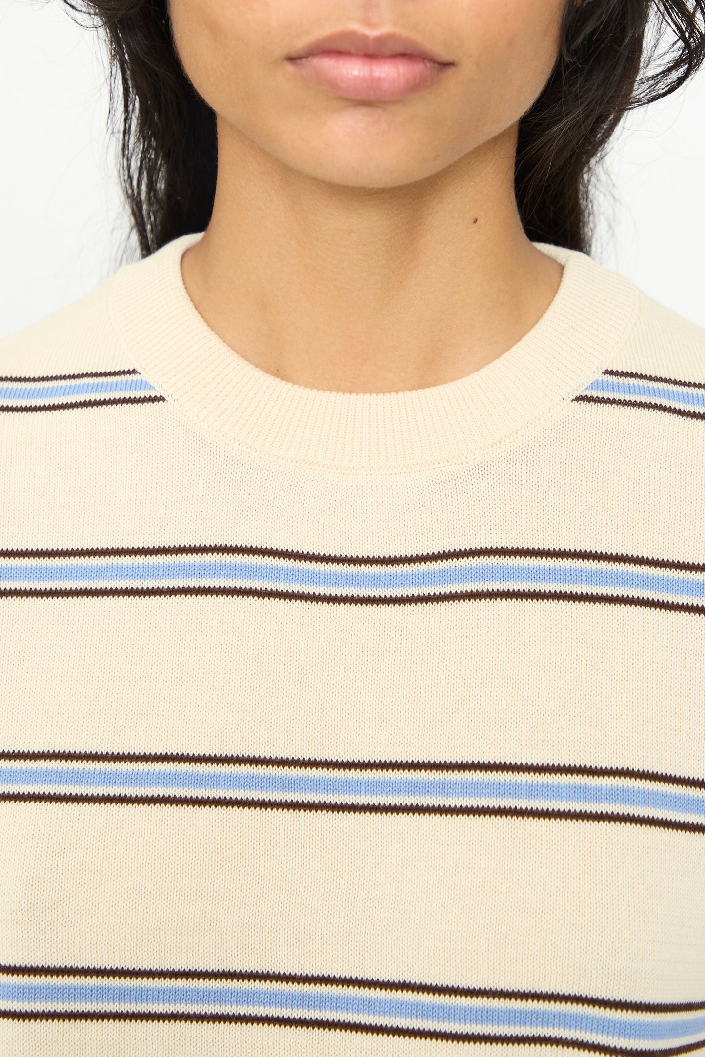 Close-up of a person’s lower face and neck, wearing an oversized fit Cotton T-Shirt in Striped by Cordera, featuring cream-colored fabric with horizontal brown and blue stripes, reminiscent of a classic striped cotton tee made in Spain.