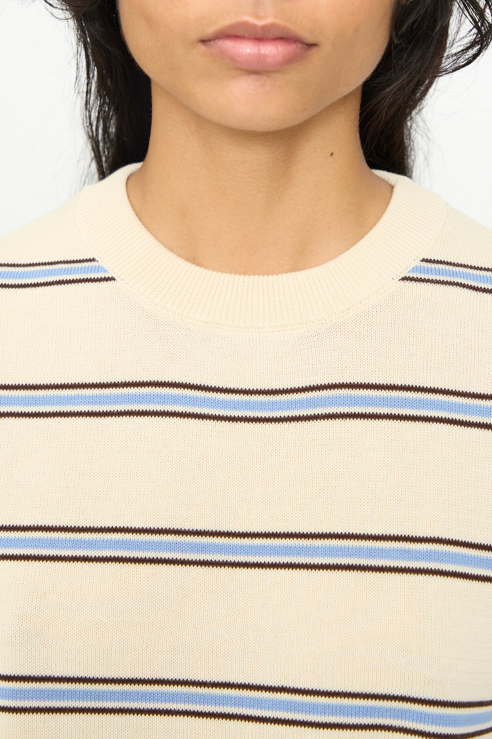 Close-up of a person’s lower face and neck, wearing an oversized fit Cotton T-Shirt in Striped by Cordera, featuring cream-colored fabric with horizontal brown and blue stripes, reminiscent of a classic striped cotton tee made in Spain.