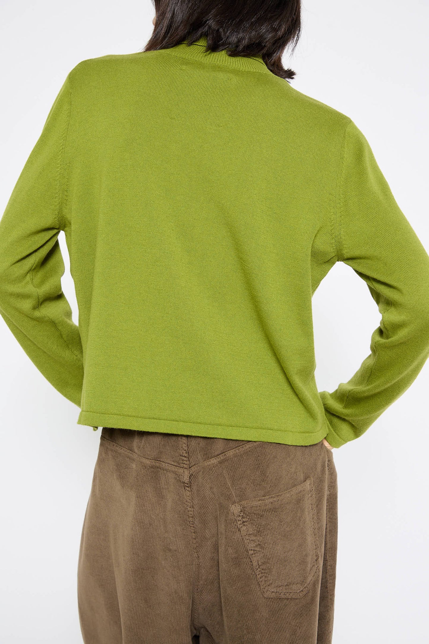 Rear view of a person wearing the Cordera Cotton and Cashmere Sweater in Woodbine paired with brown corduroy pants, with their hands on their hips.