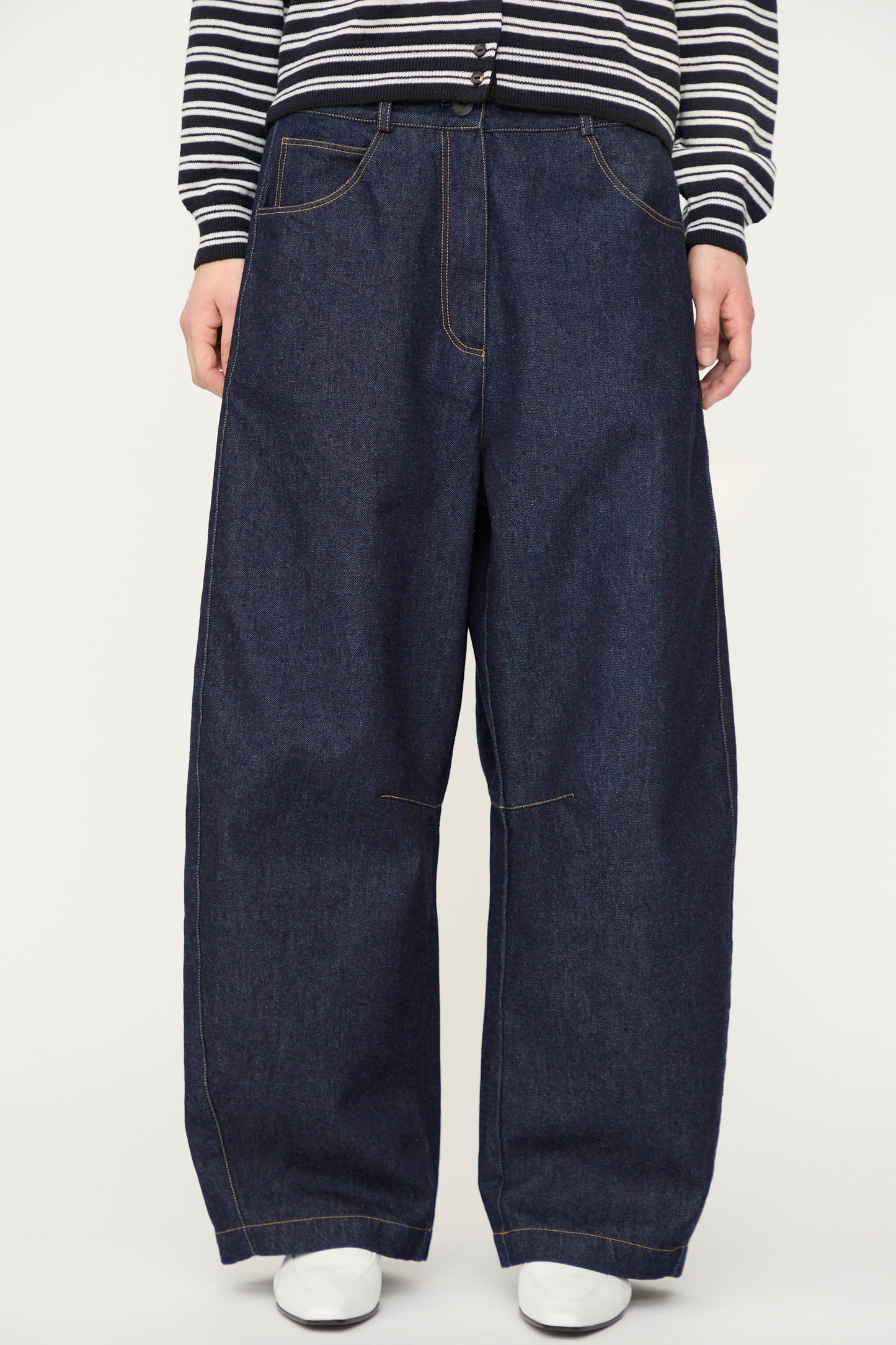 A person wears Cordera's Curved Baggy Jean in dark blue denim, paired with a black-and-white striped long-sleeve top and white shoes. The photo is cropped from the shoulders down.